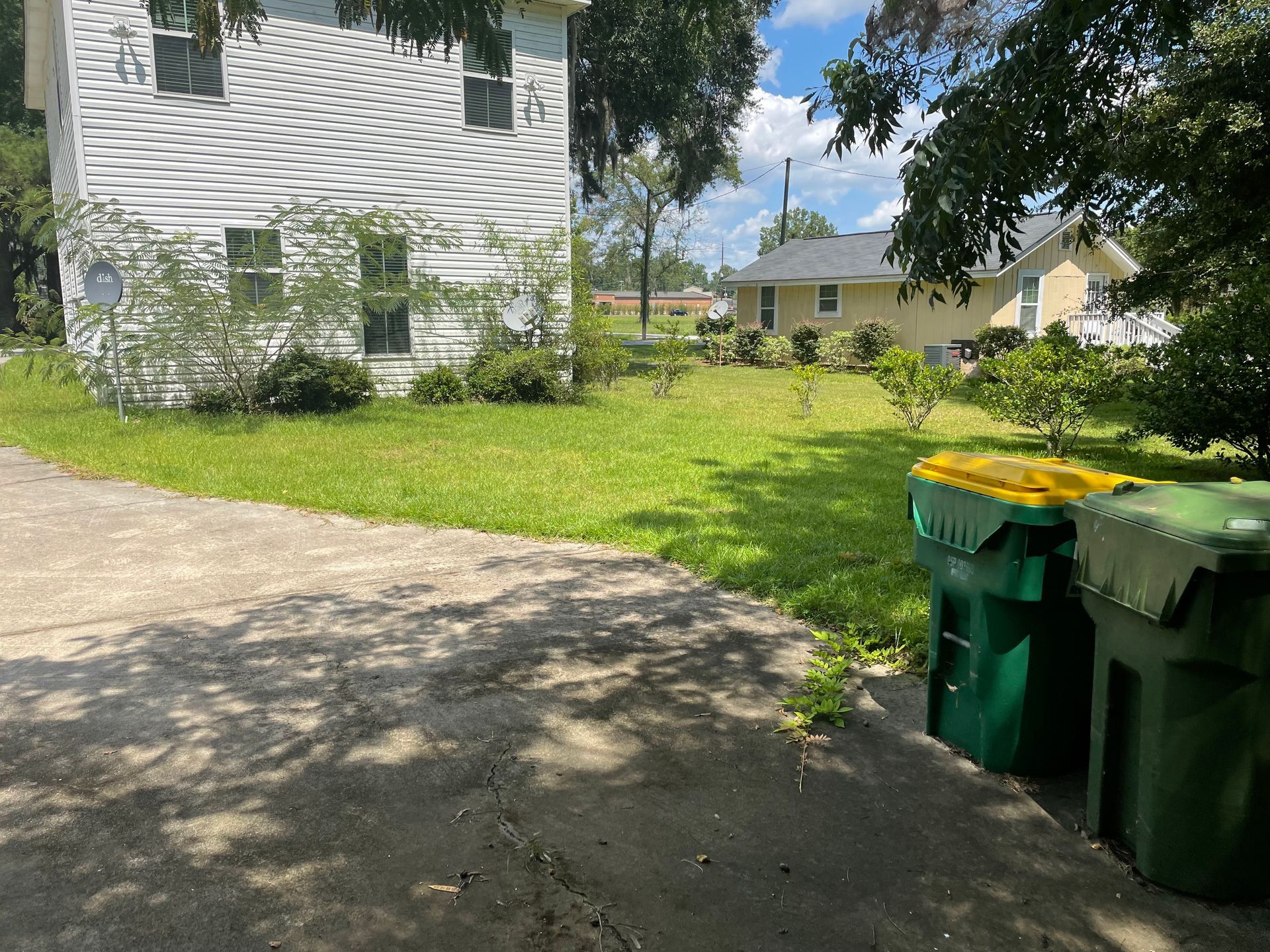 Two green trash cans are sitting on the sidewalk in front of a house.
