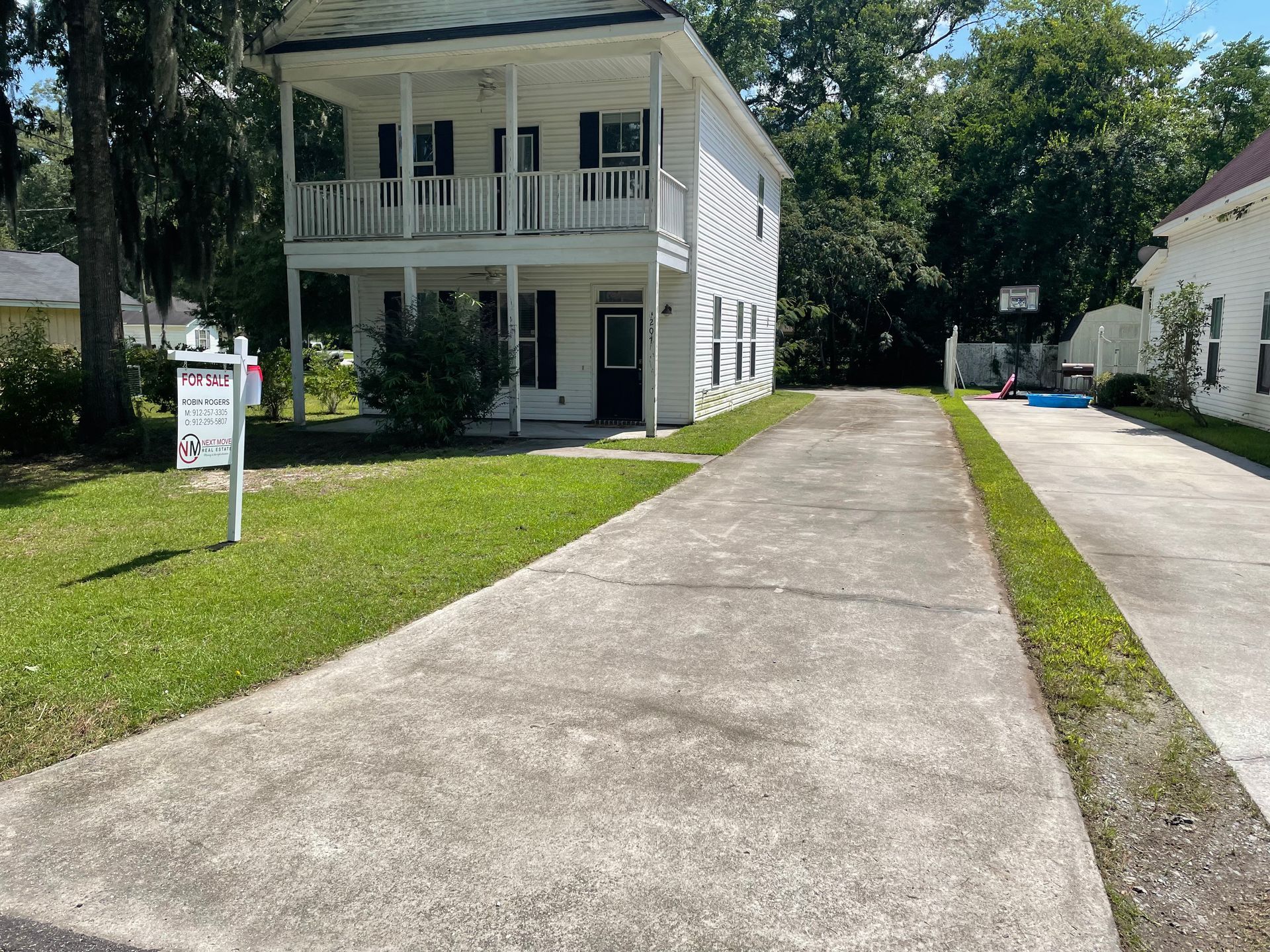 A white house with a driveway and a for sale sign in front of it.