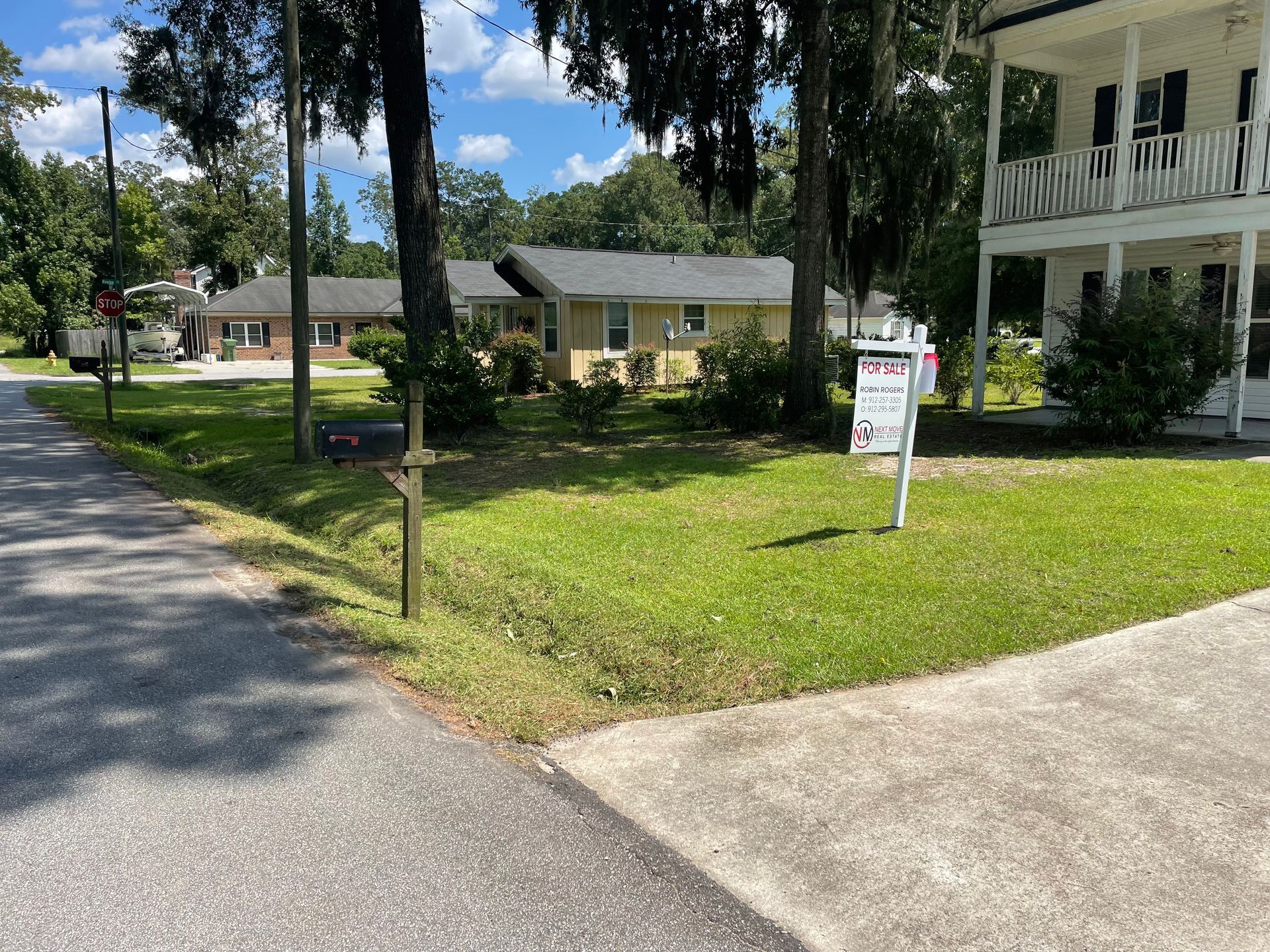 A house for sale is sitting on the corner of a street.