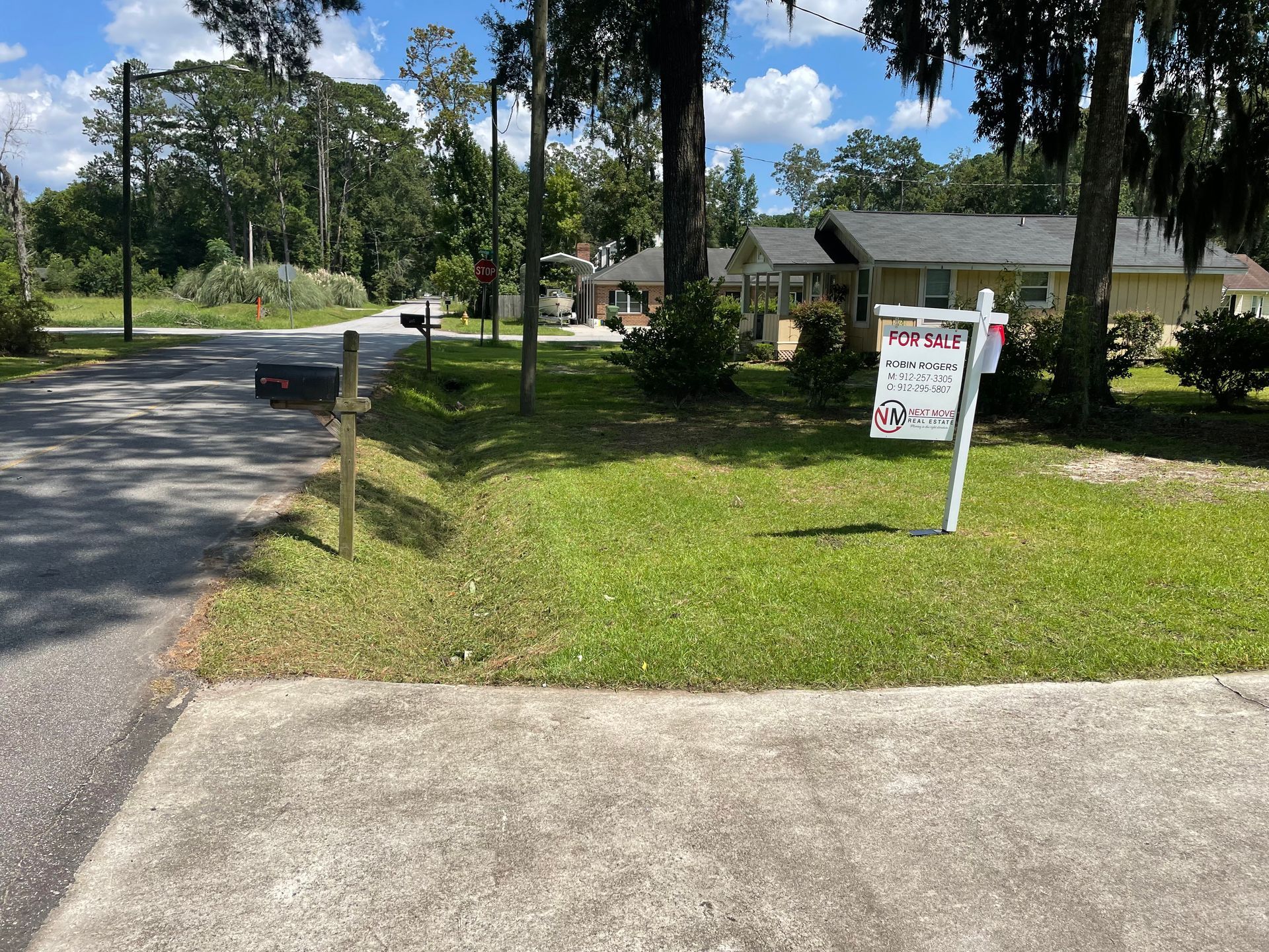A for sale sign is sitting in the grass in front of a house.
