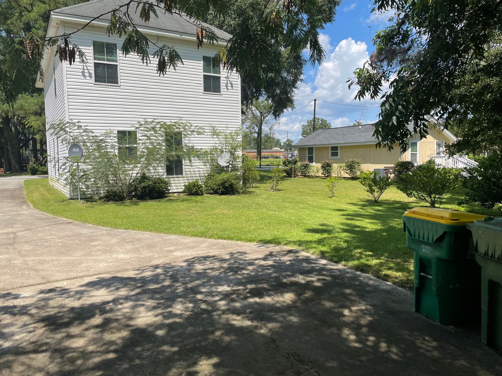 A white house with a green trash can in front of it.