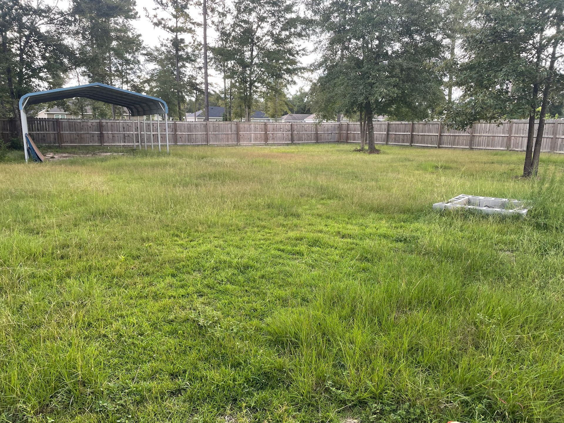 A large grassy field with a fence and trees in the background.