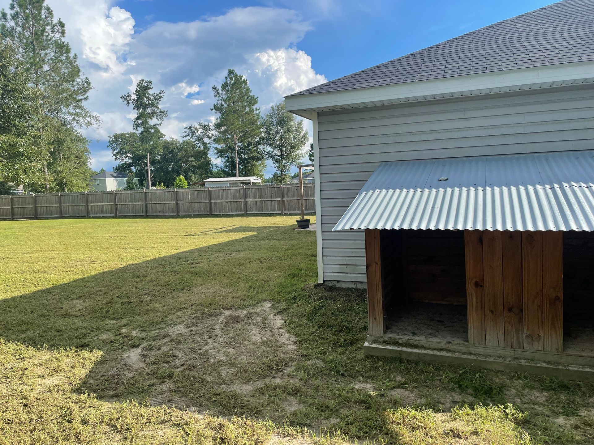 A white house with a metal roof and a wooden shed in the backyard.