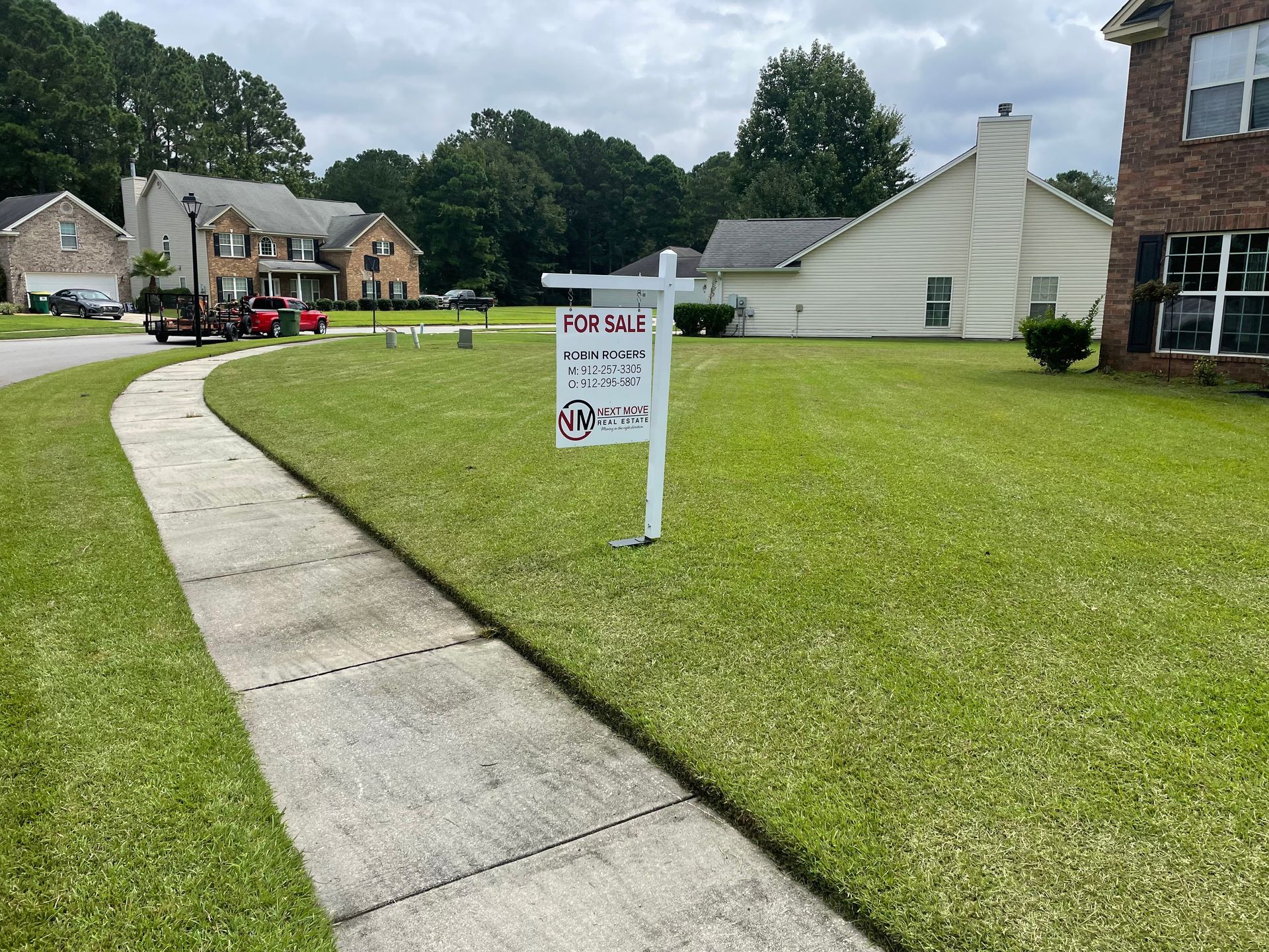 A for sale sign is sitting on the sidewalk in front of a house.