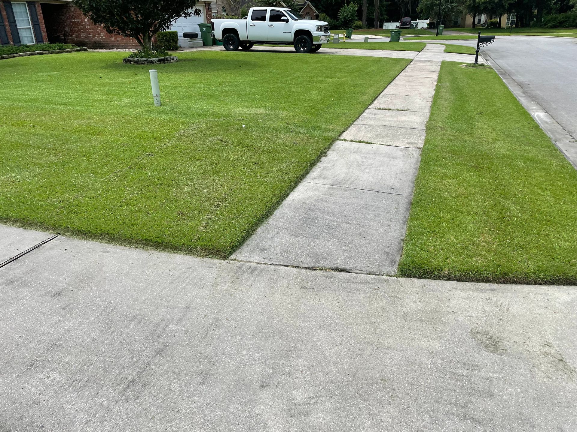 A white truck is parked in the grass next to a sidewalk.