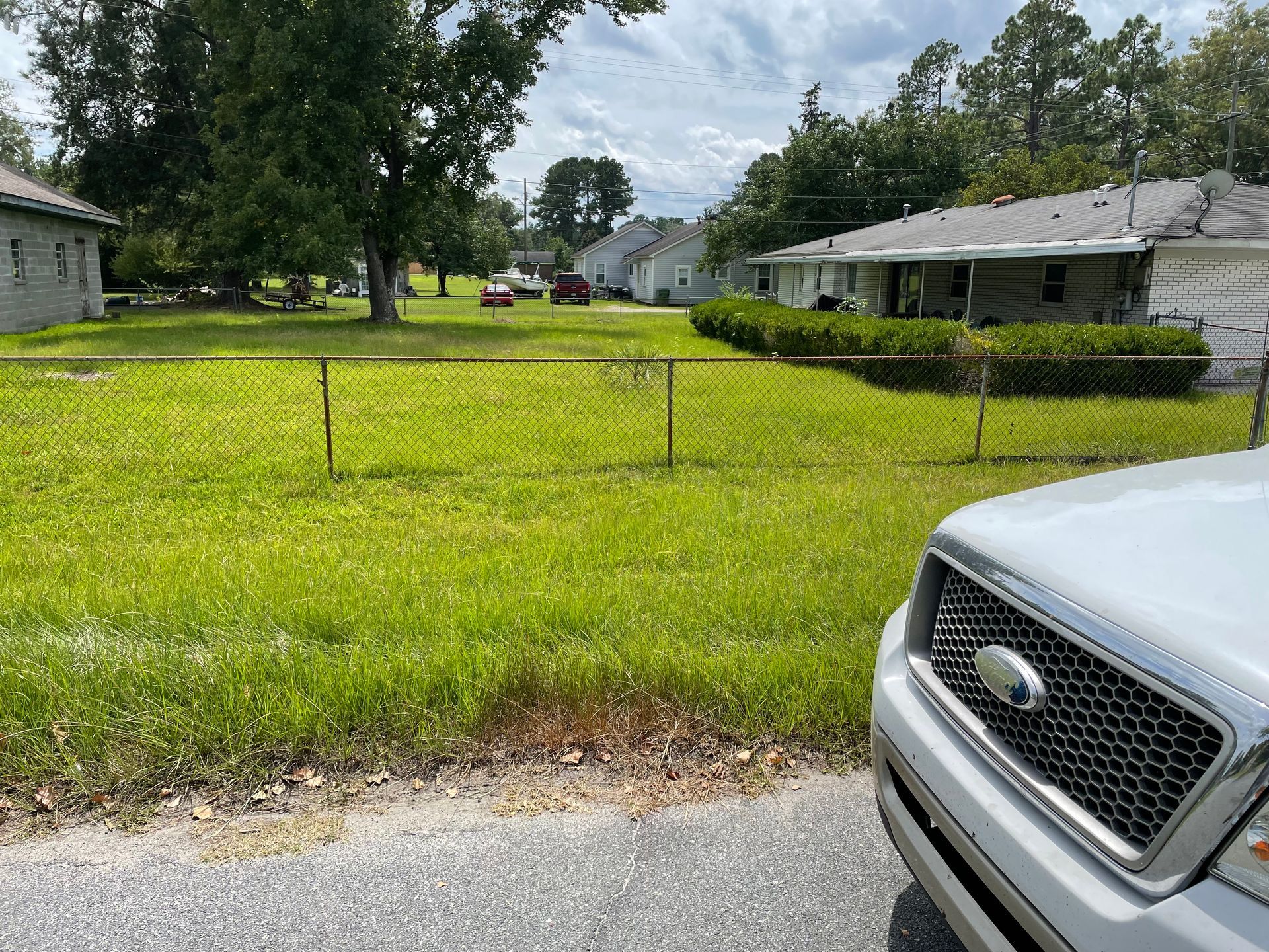 A white ford truck is parked in front of a lush green field.