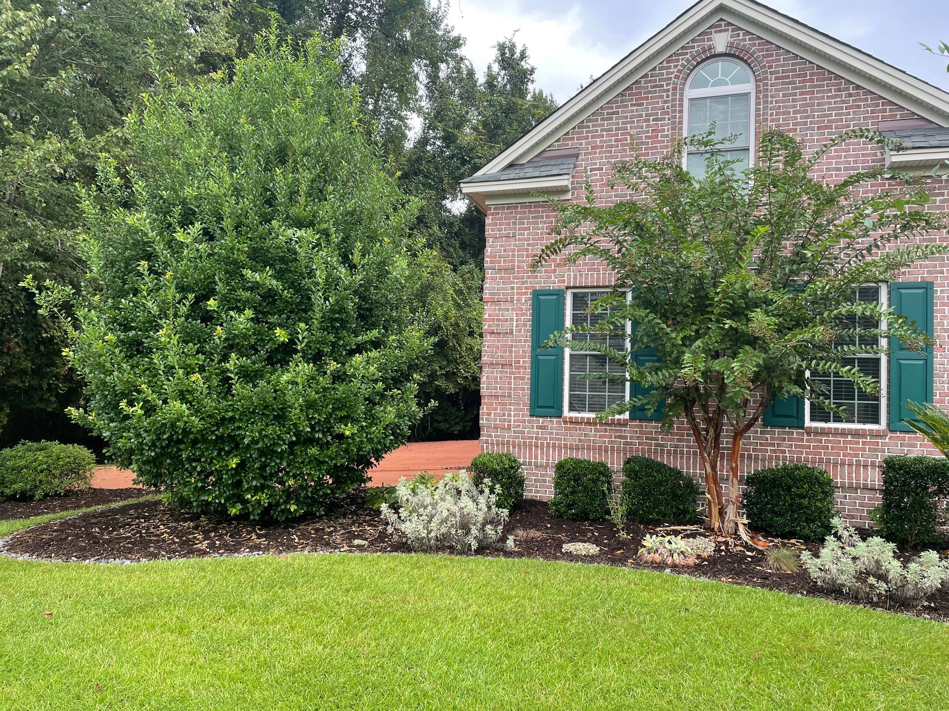A brick house with green shutters and a large lawn in front of it.