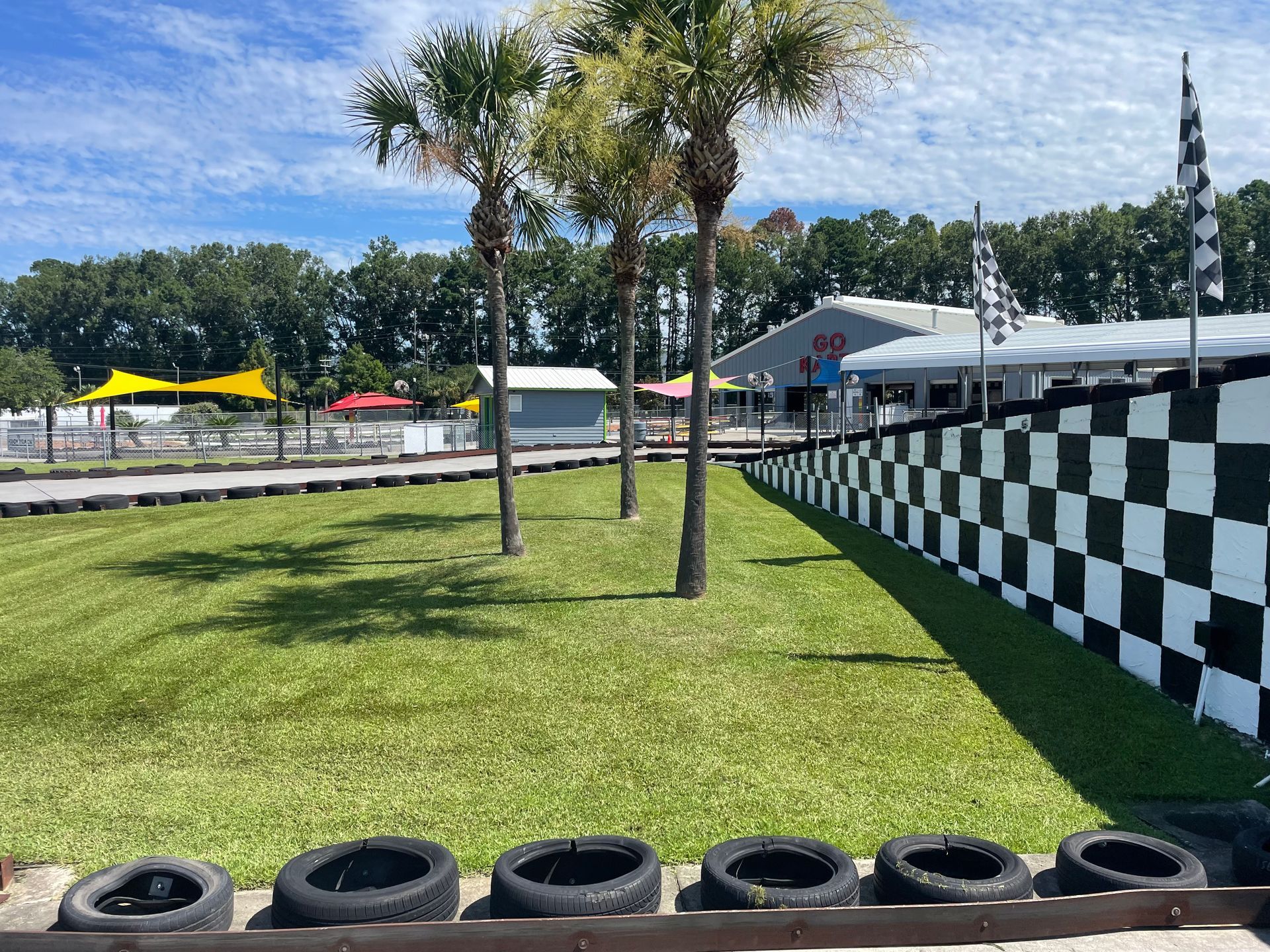 A race track with a checkered wall and tires in the grass.