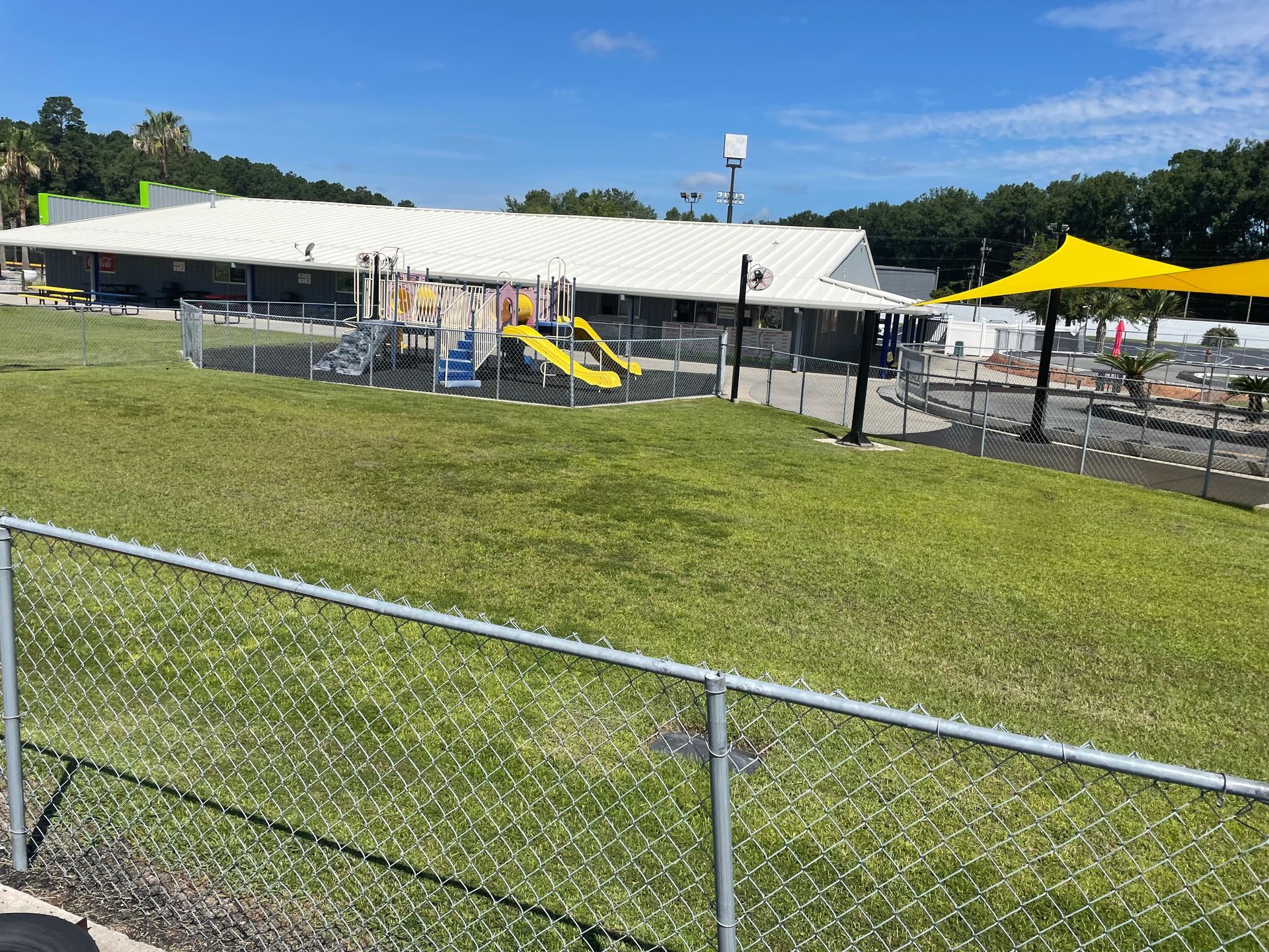 A playground with a yellow slide and umbrellas is behind a chain link fence.