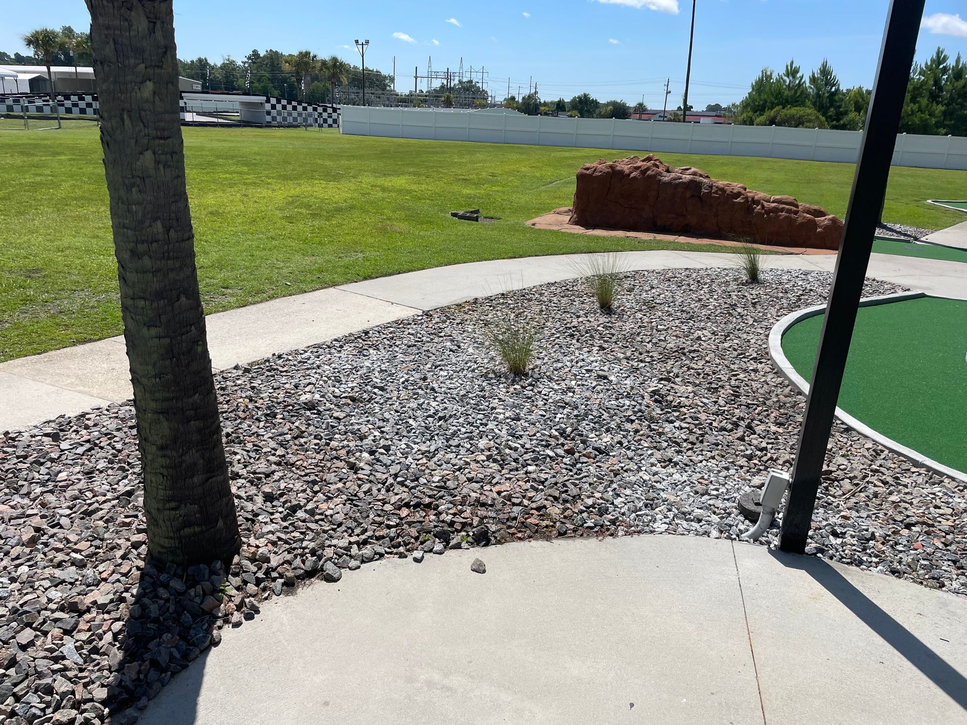 A concrete walkway leading to a golf course with a palm tree in the background