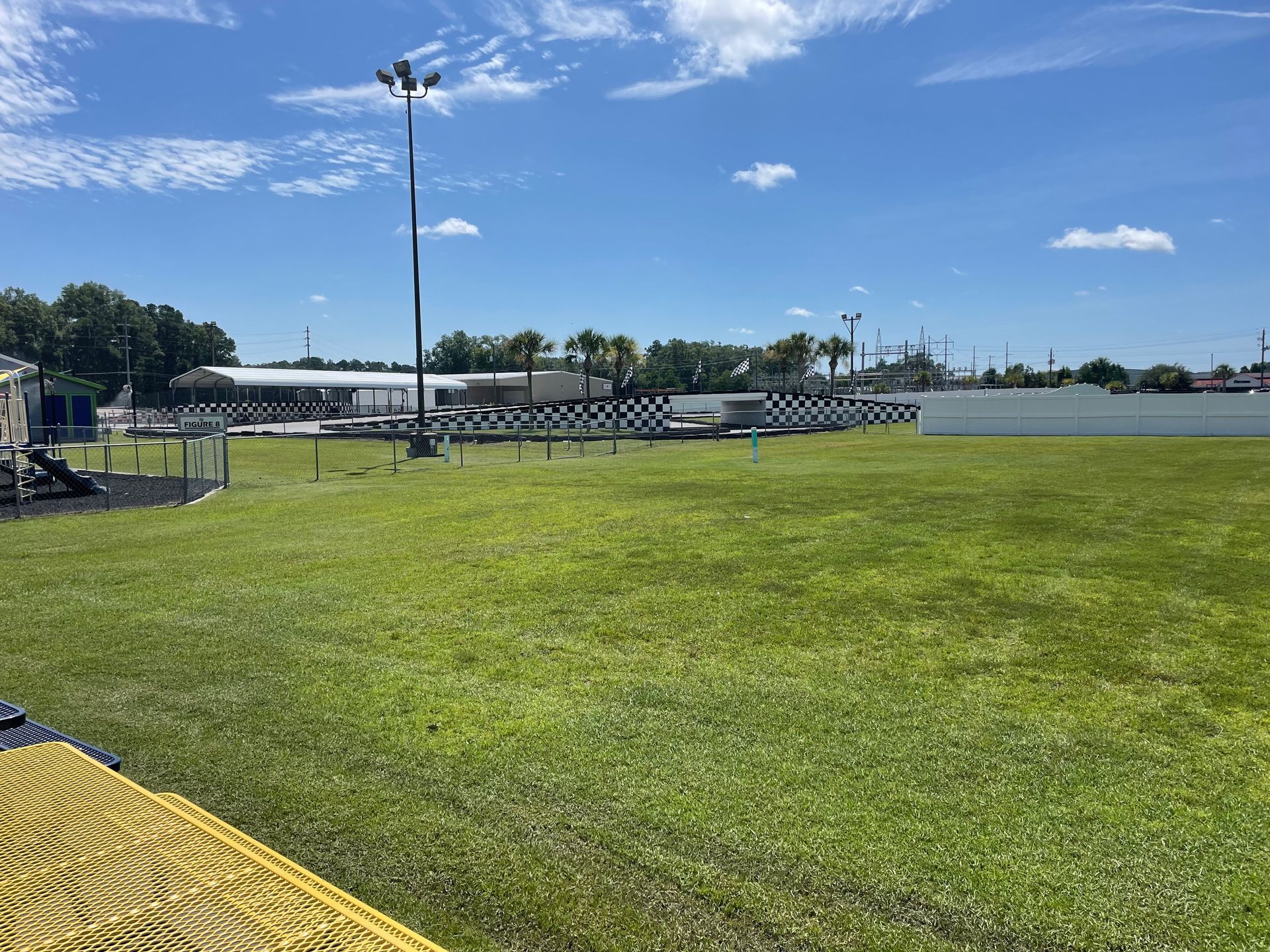 A large grassy field with a playground in the background on a sunny day.