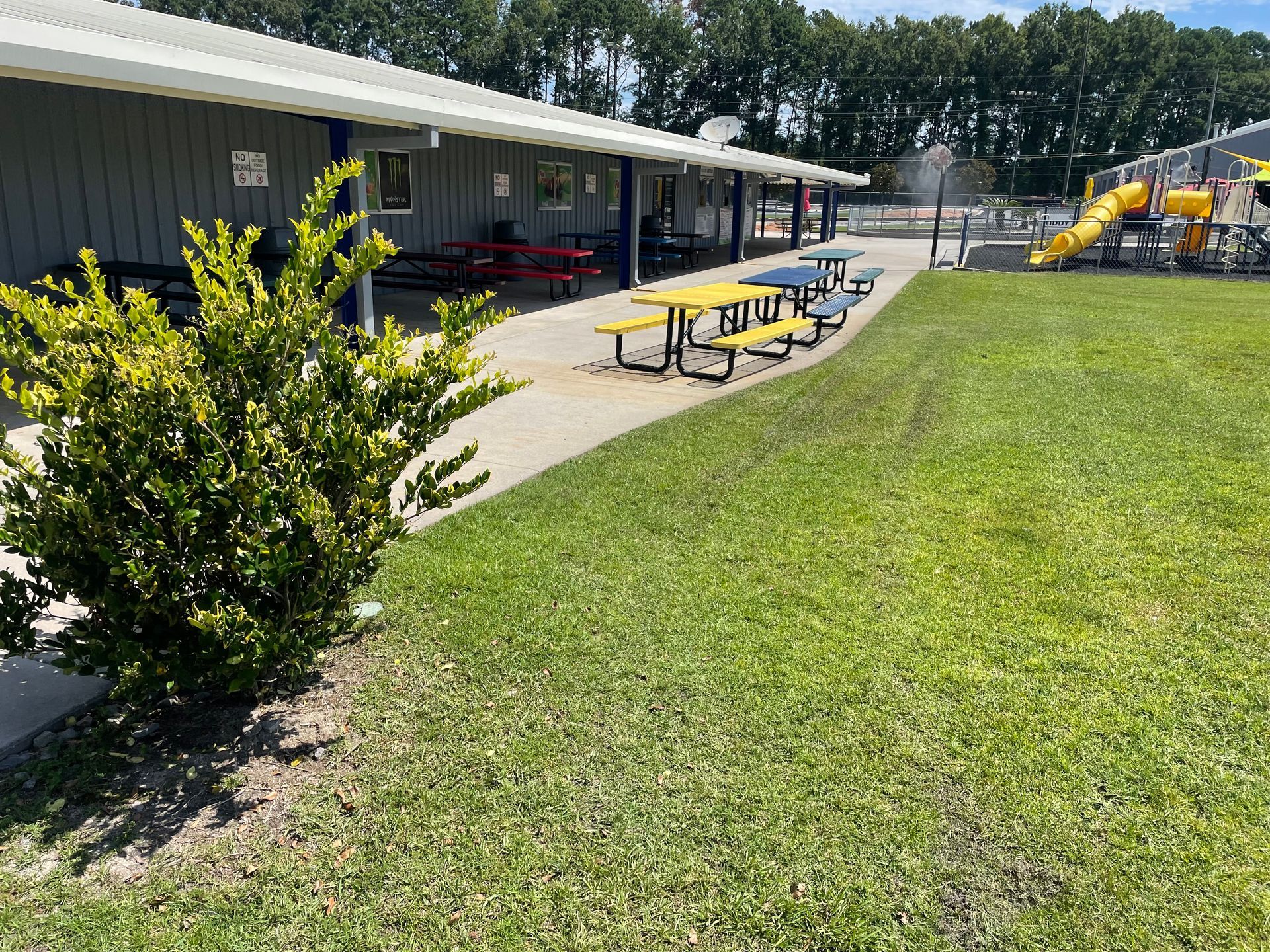 A picnic area with tables and benches in front of a building and a playground.