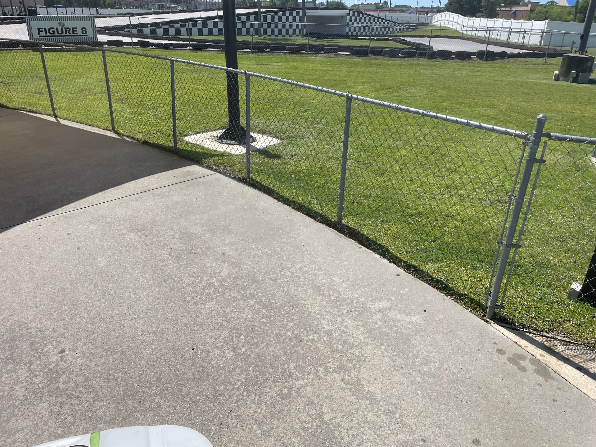 A chain link fence surrounds a parking lot with a race track in the background.
