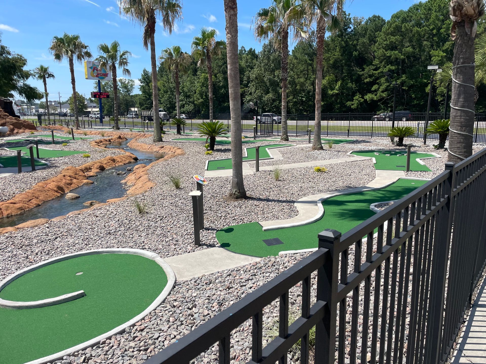 A fence surrounds a mini golf course with palm trees in the background