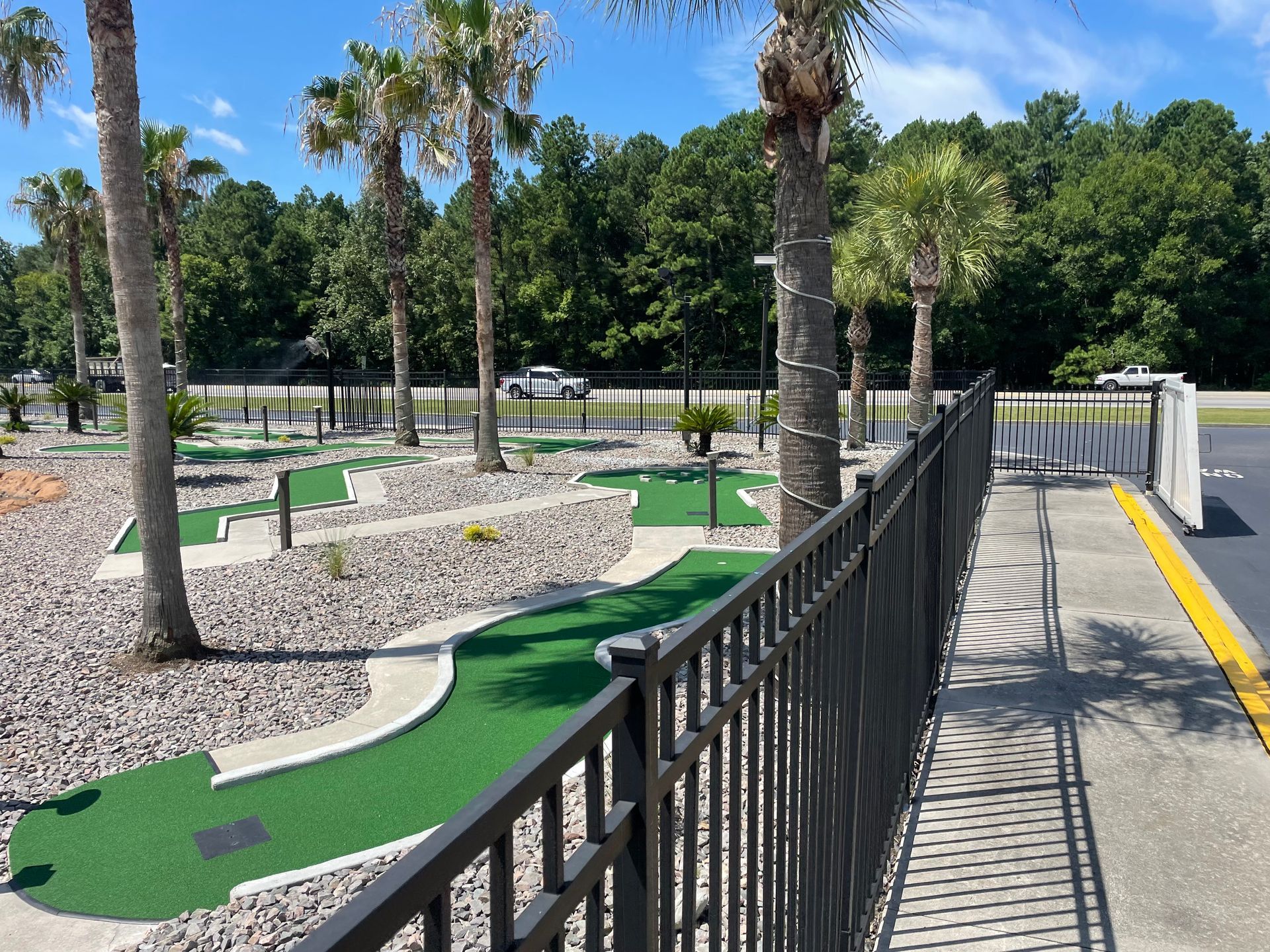 A fence surrounds a mini golf course with palm trees in the background