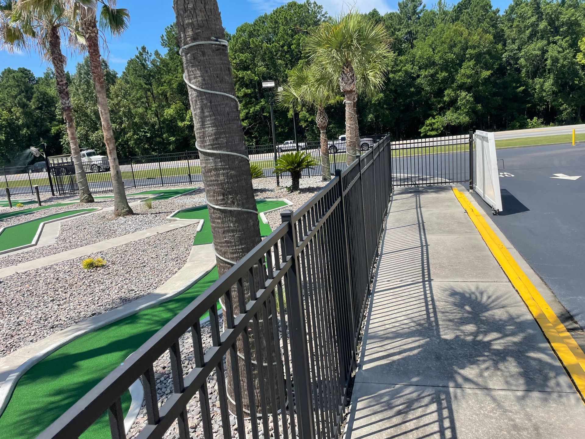 A fence surrounds a mini golf course with palm trees in the background.