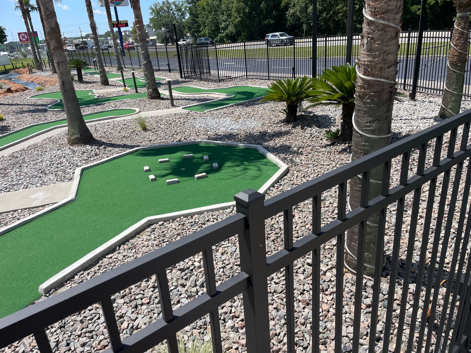 A mini golf course is behind a fence with palm trees in the background