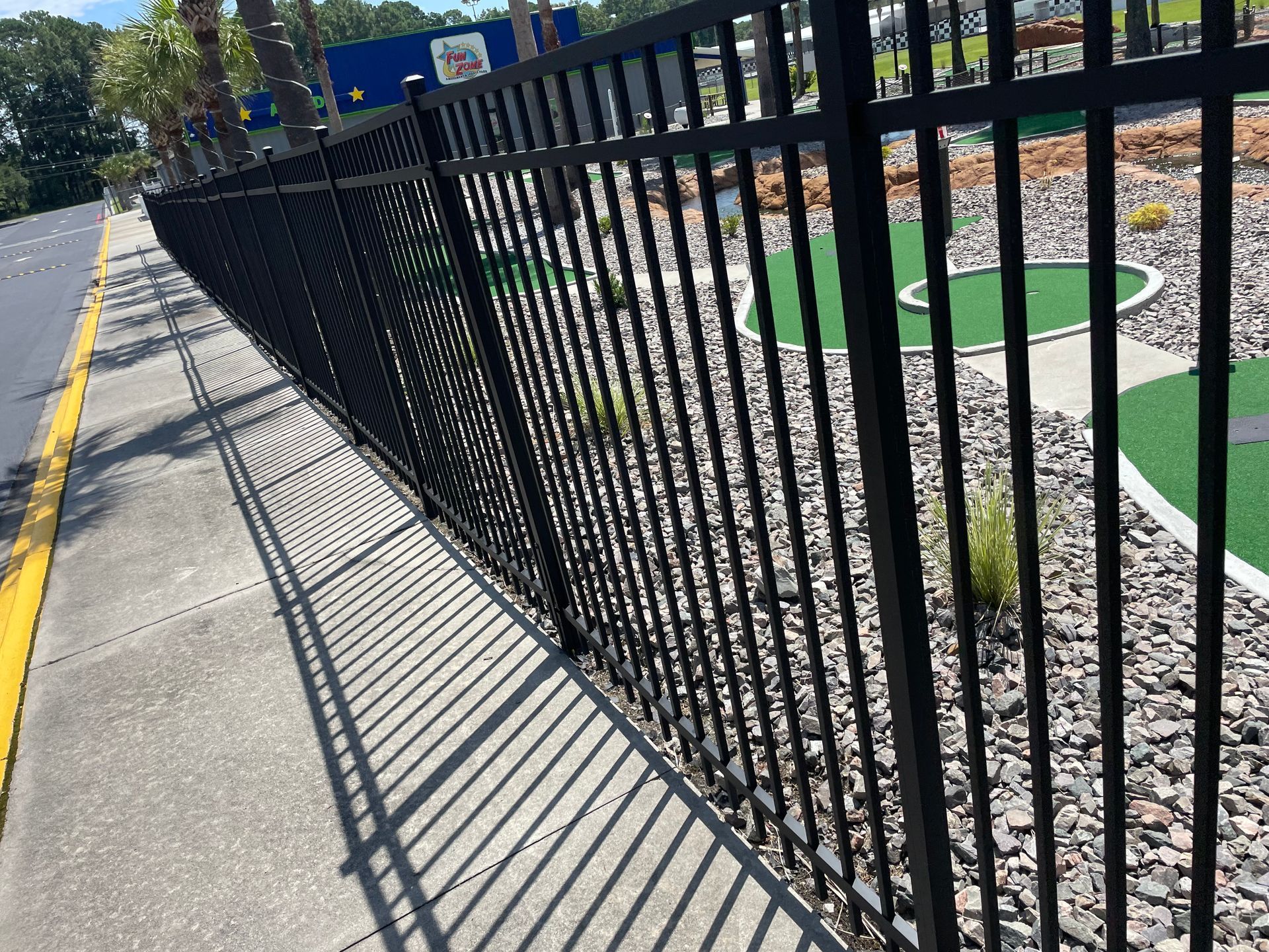 A black metal fence along a sidewalk next to a golf course.