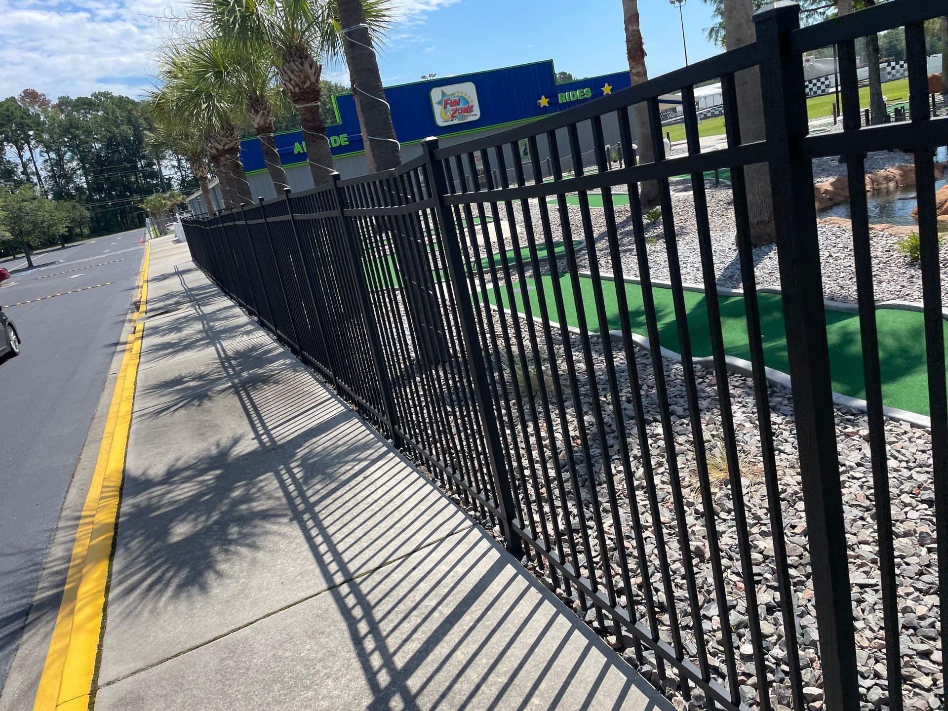 A black metal fence along a sidewalk next to a golf course.