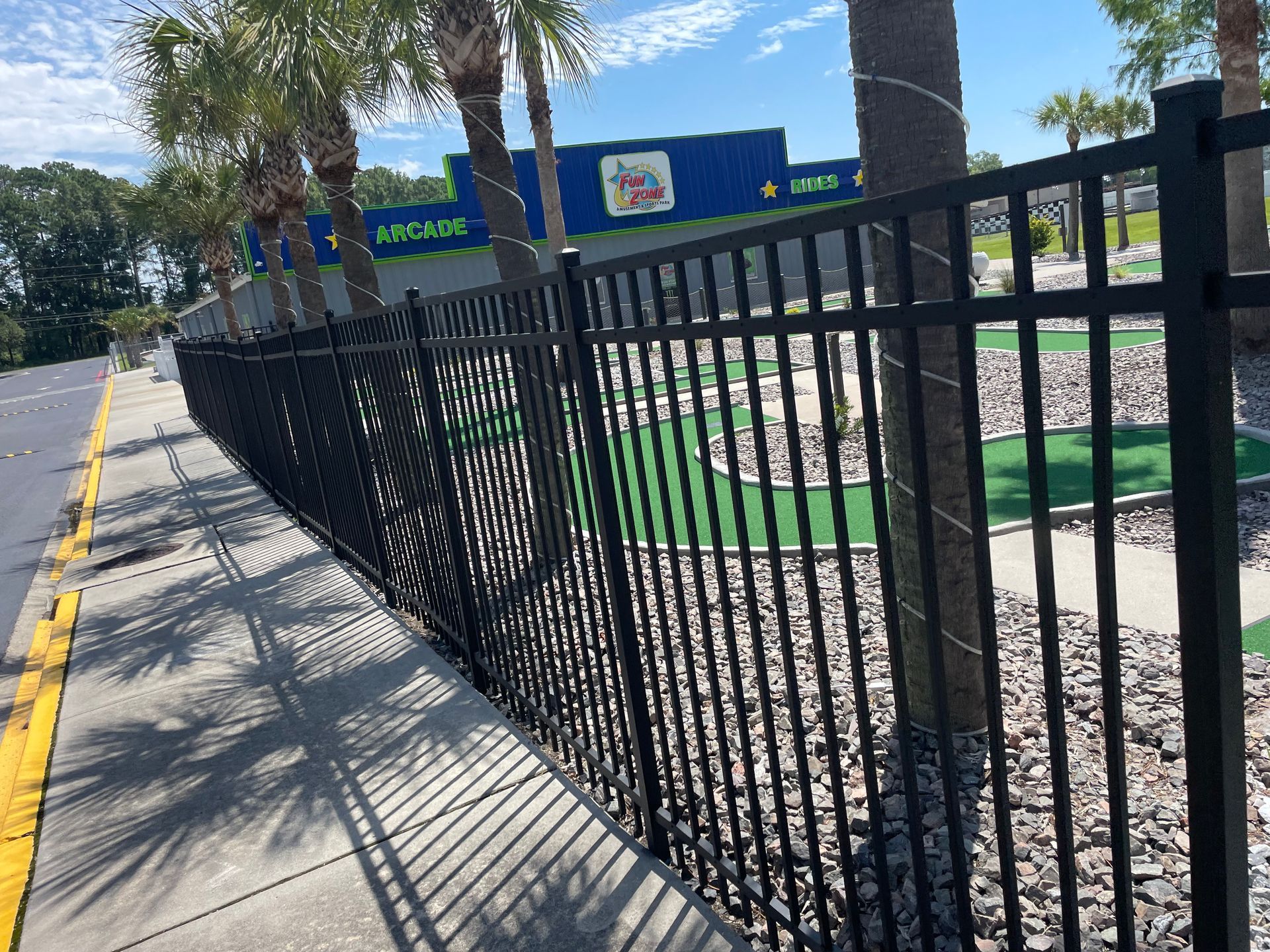A black fence along a sidewalk next to a mini golf course.