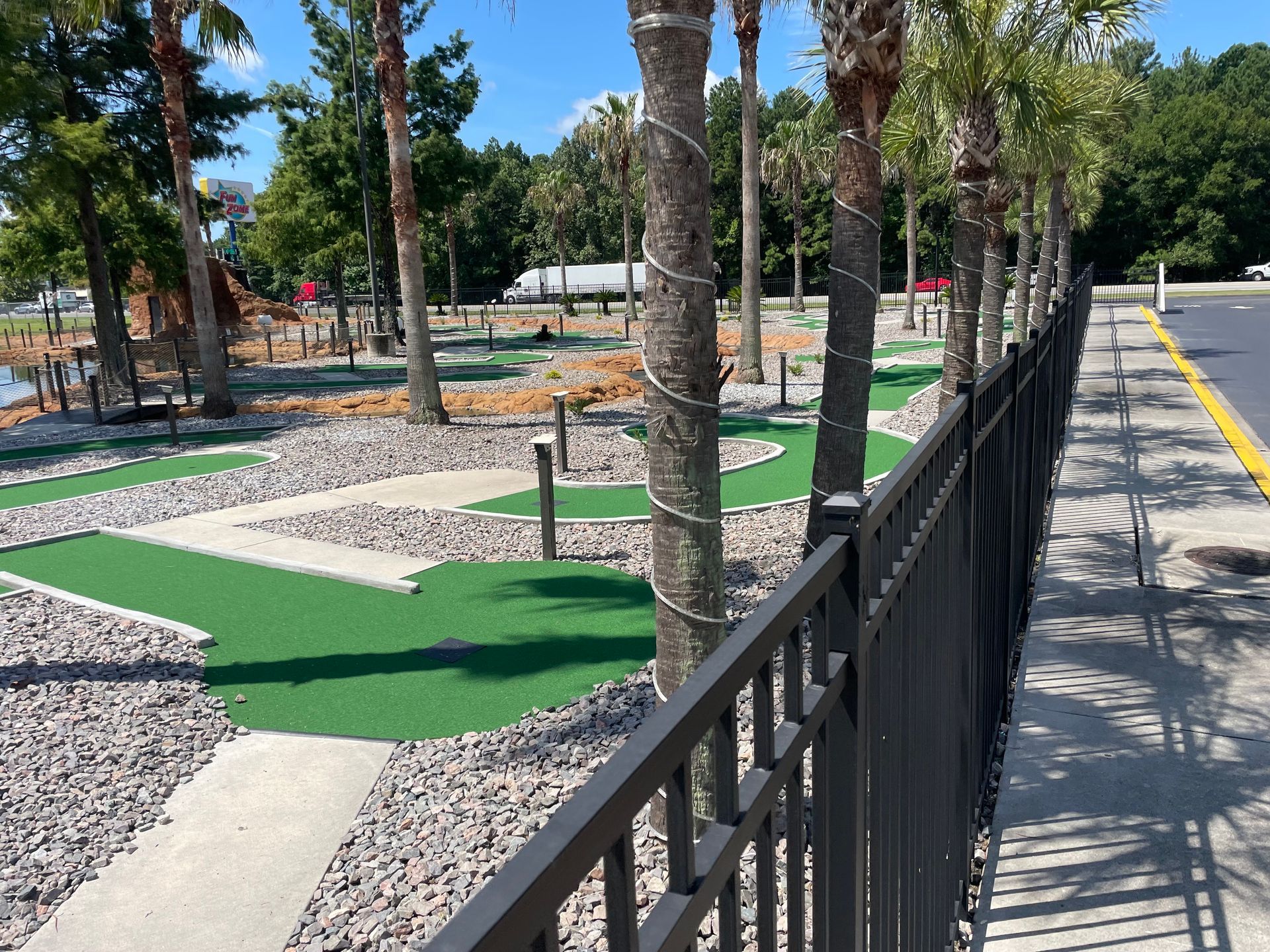 A fence surrounds a mini golf course with palm trees in the background