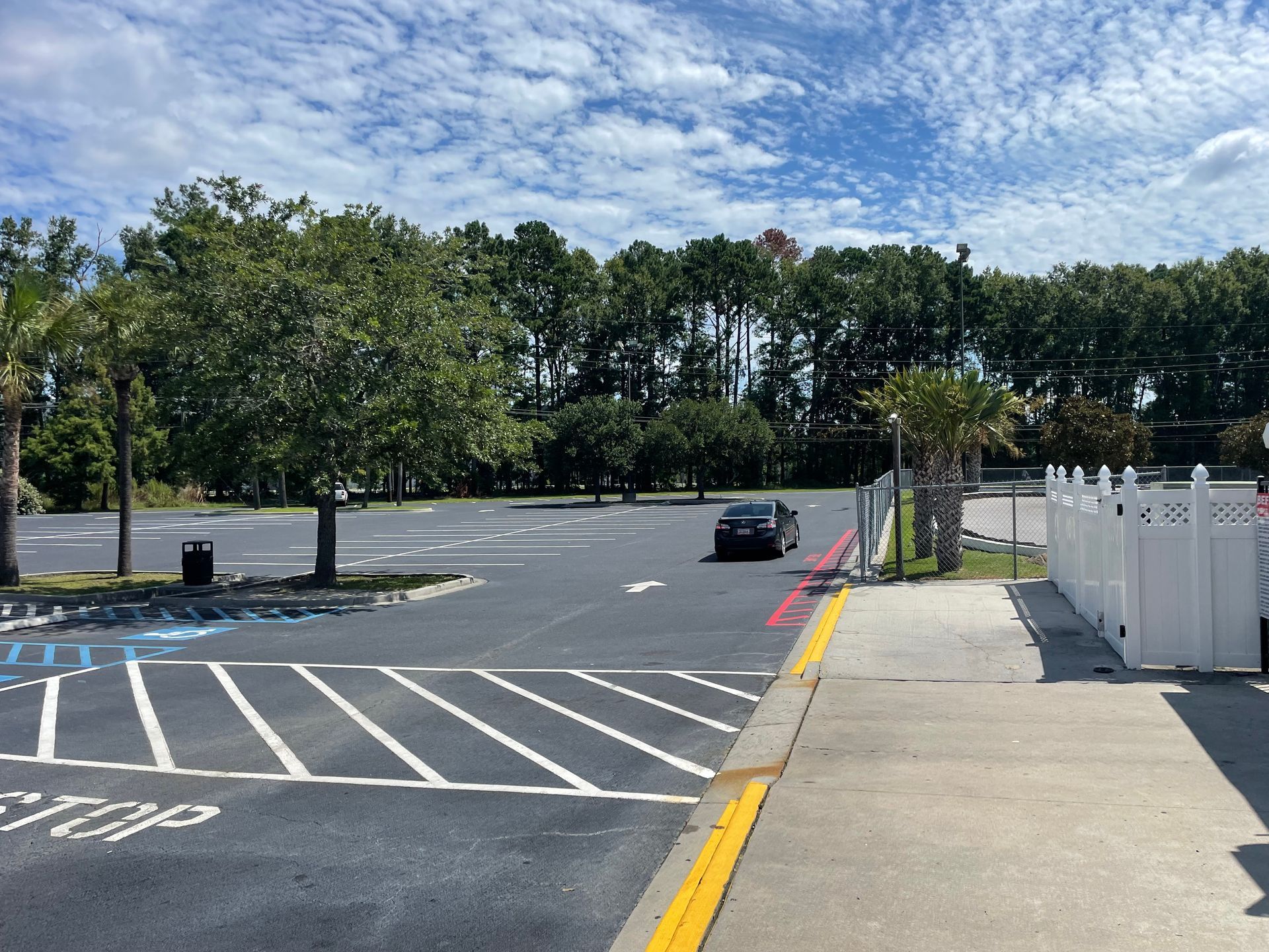 A car is driving down a parking lot next to a sidewalk.