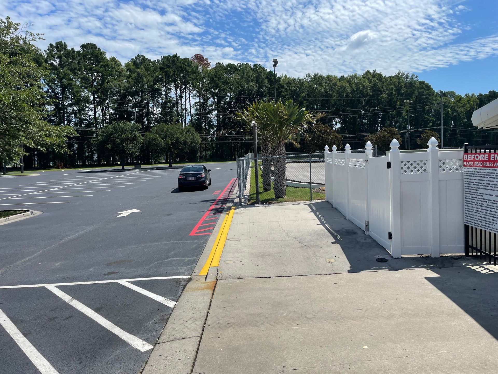 A car is driving down a street next to a white fence.