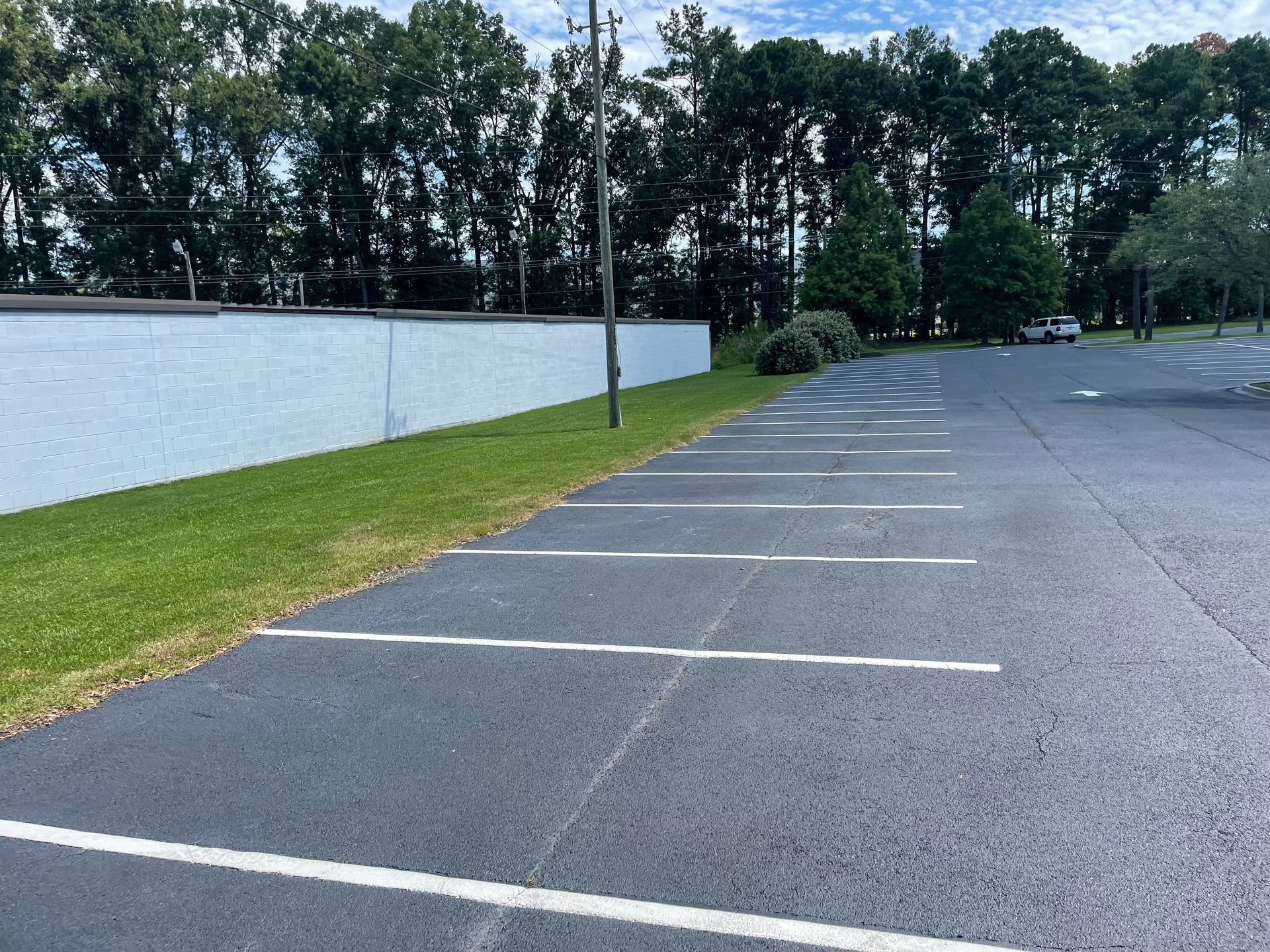 A parking lot with a white wall and trees in the background