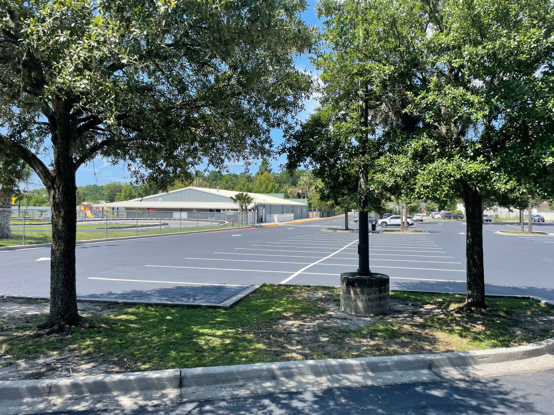 A parking lot with trees in the foreground and a building in the background.