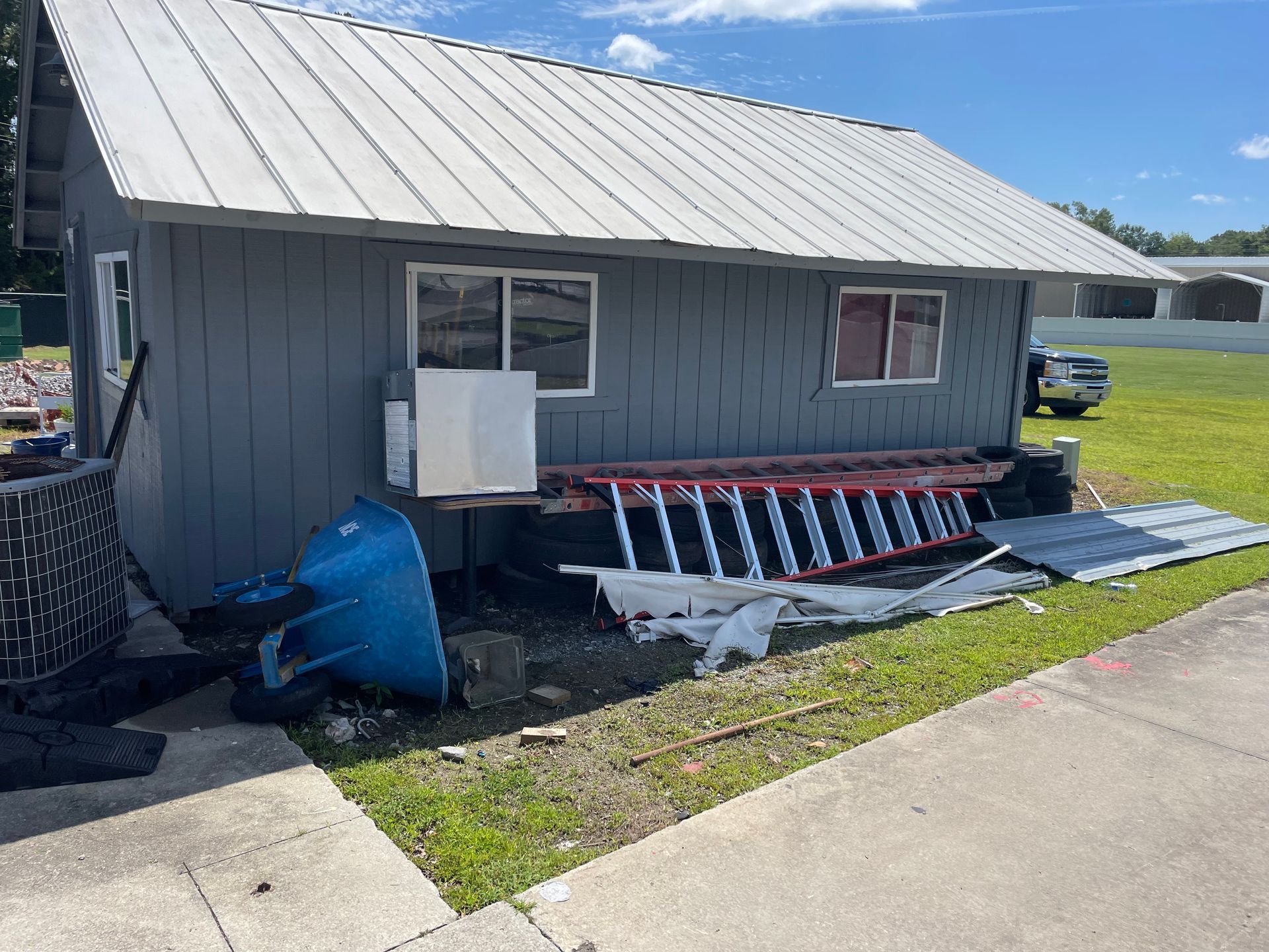 A gray house with a metal roof and a ladder in front of it.