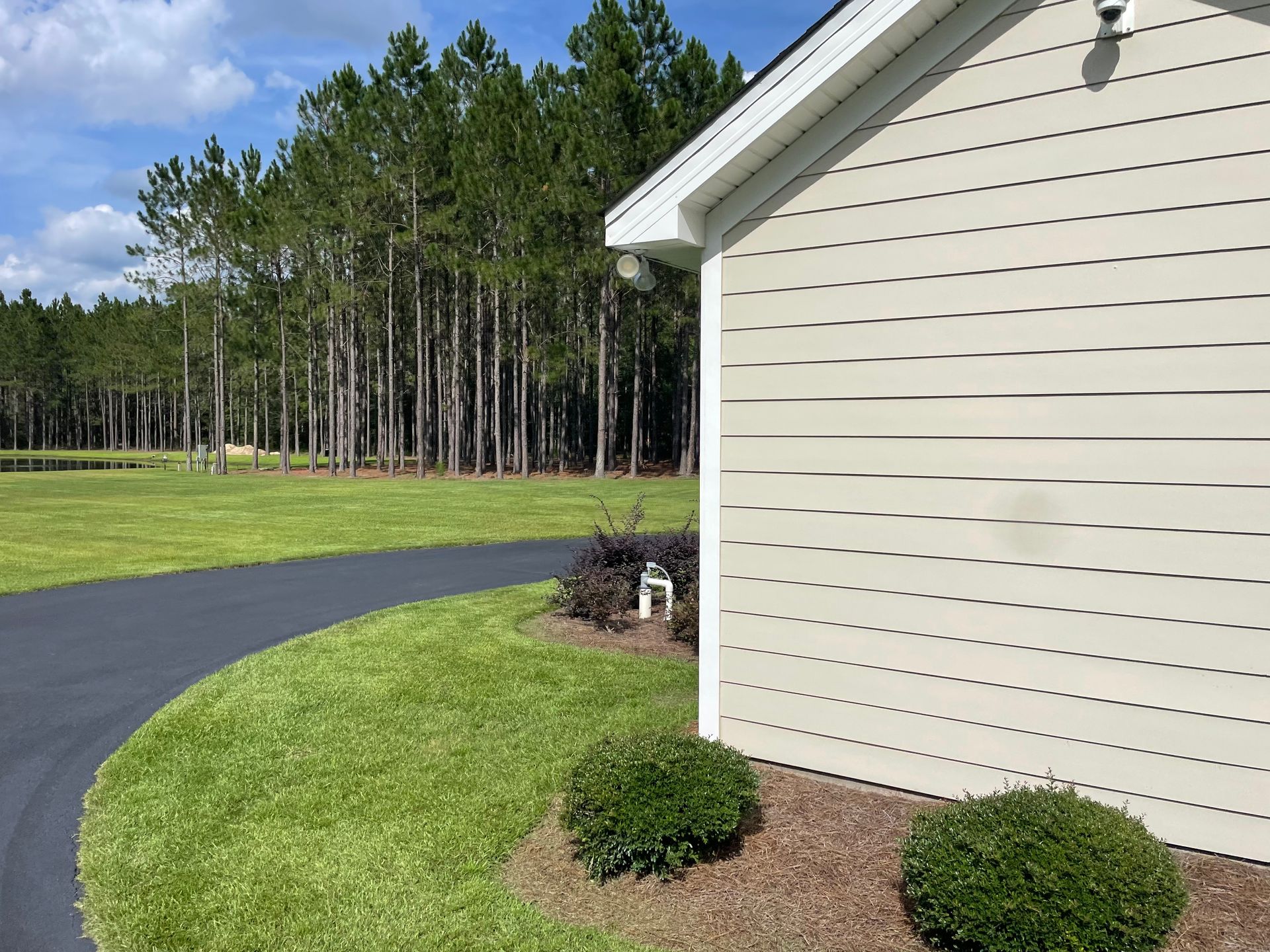 A house with a driveway leading to it and trees in the background.