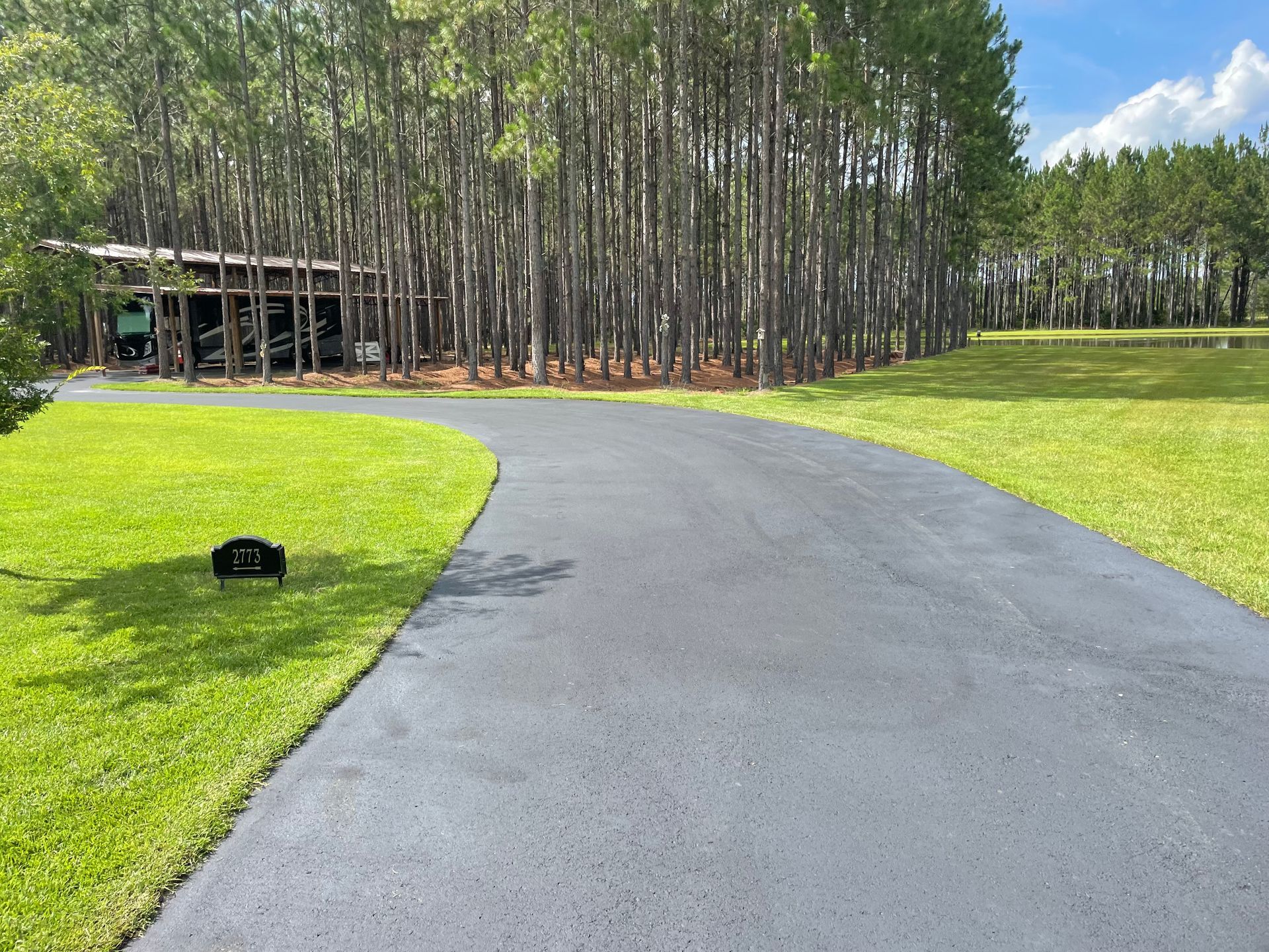 A driveway leading to a house surrounded by trees and grass.