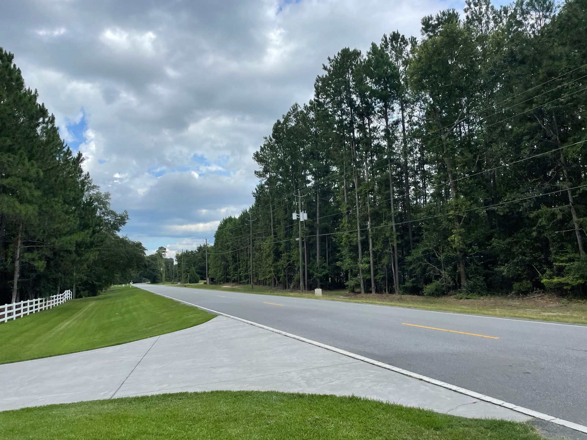 A road with trees on the side of it and a white fence