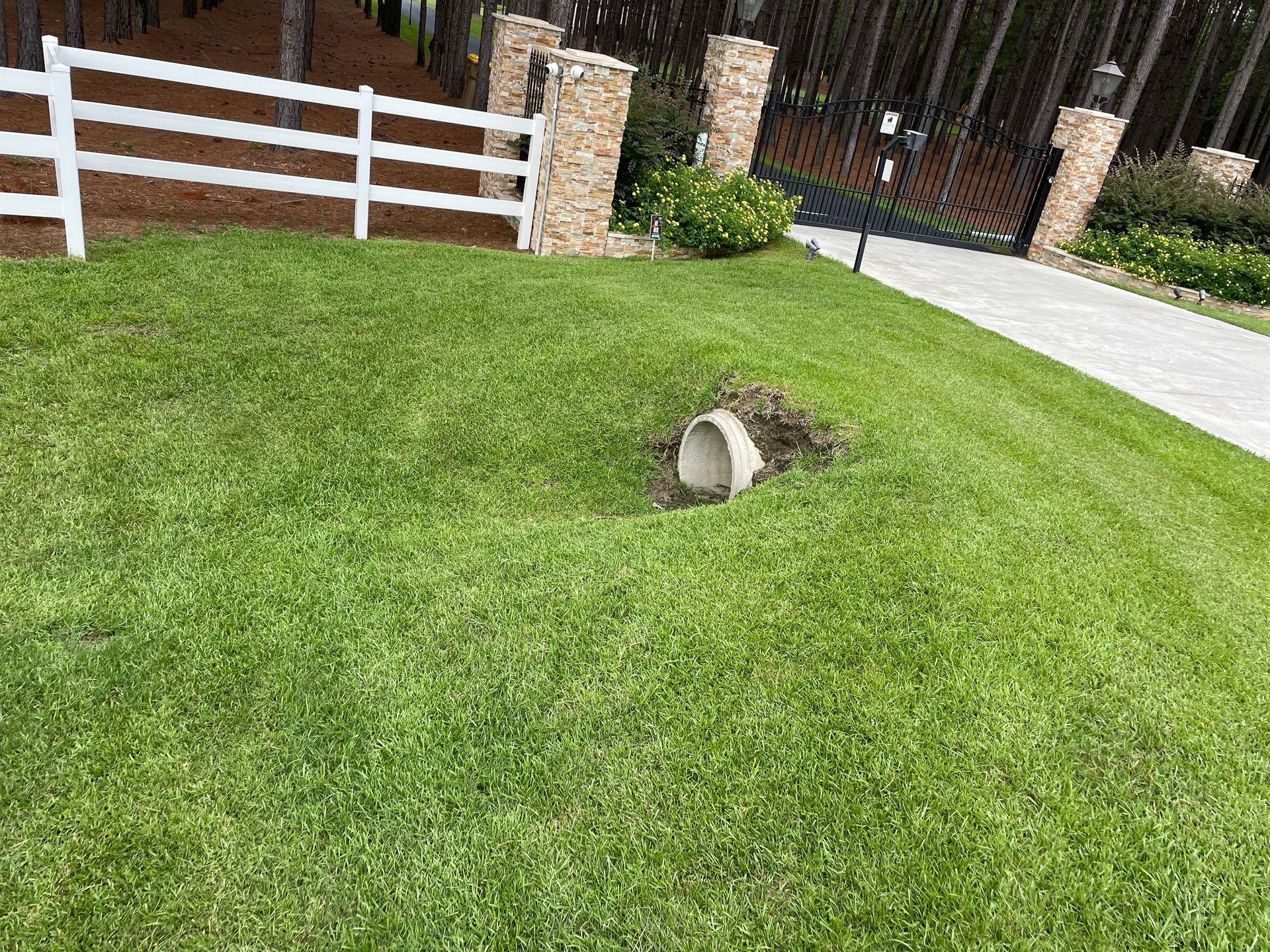 A drain pipe is sitting in the middle of a lush green lawn next to a white fence.