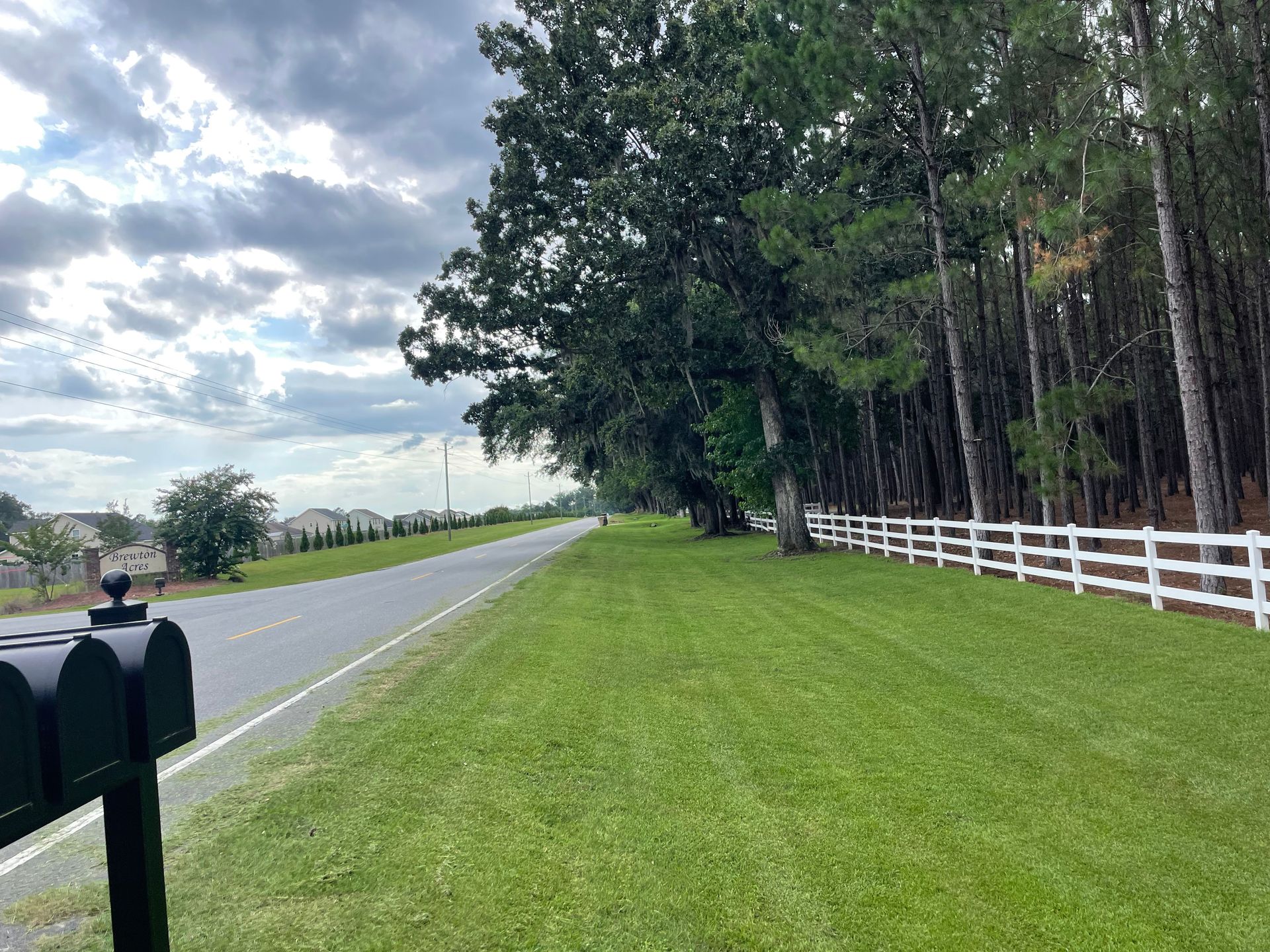 A mailbox is sitting on the side of a road next to a white fence.