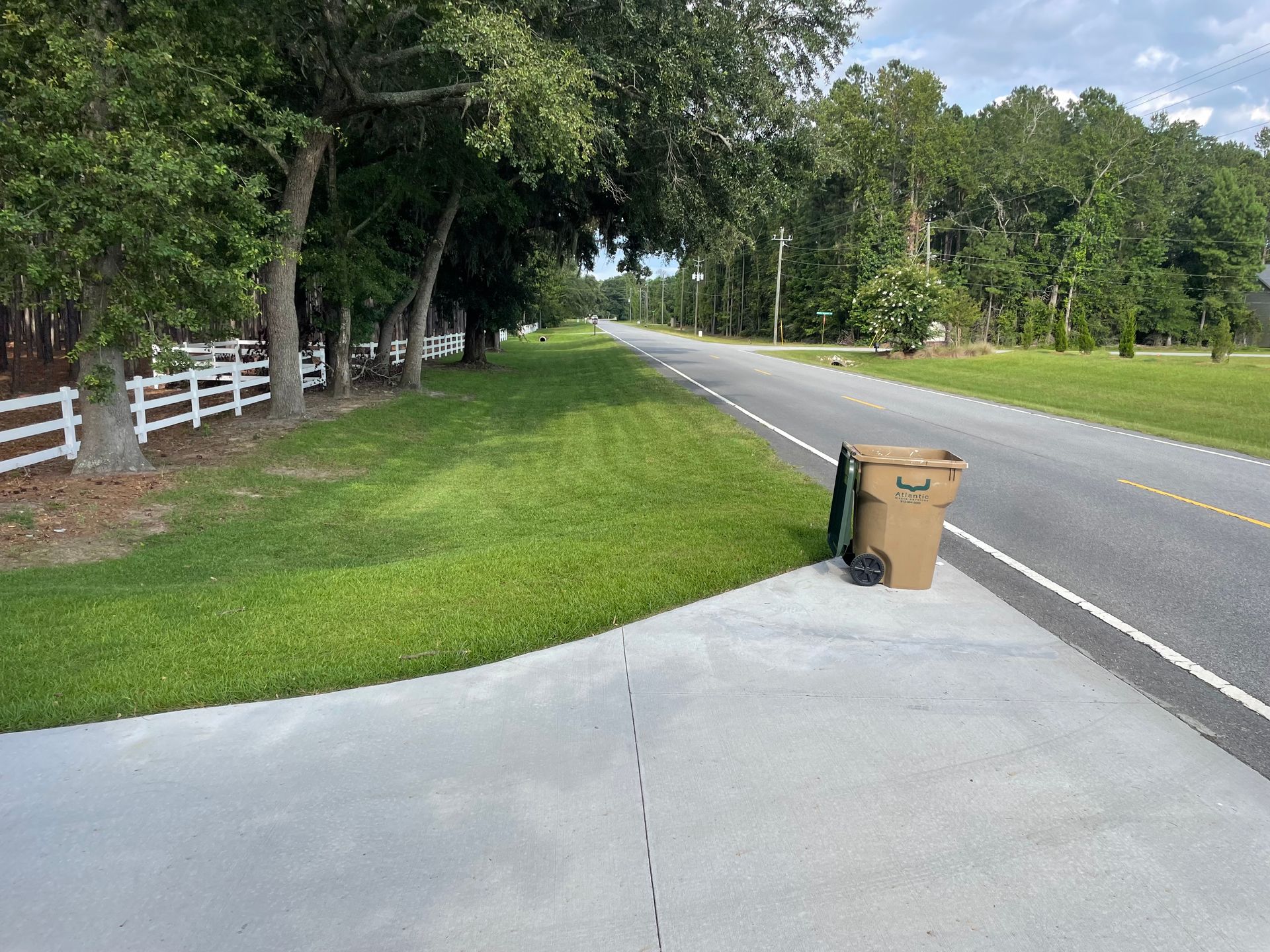 A trash can is sitting on the side of a road.