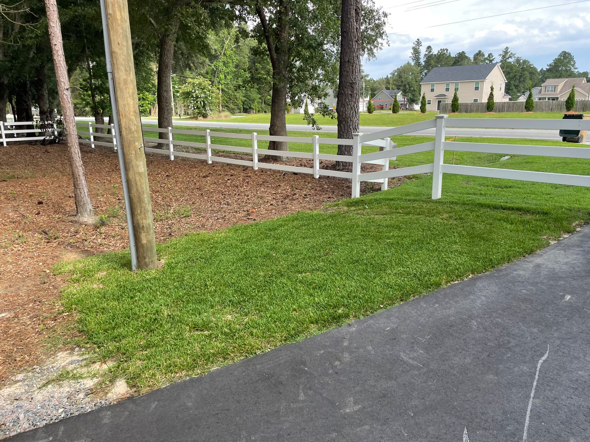 A white fence surrounds a lush green field next to a road.