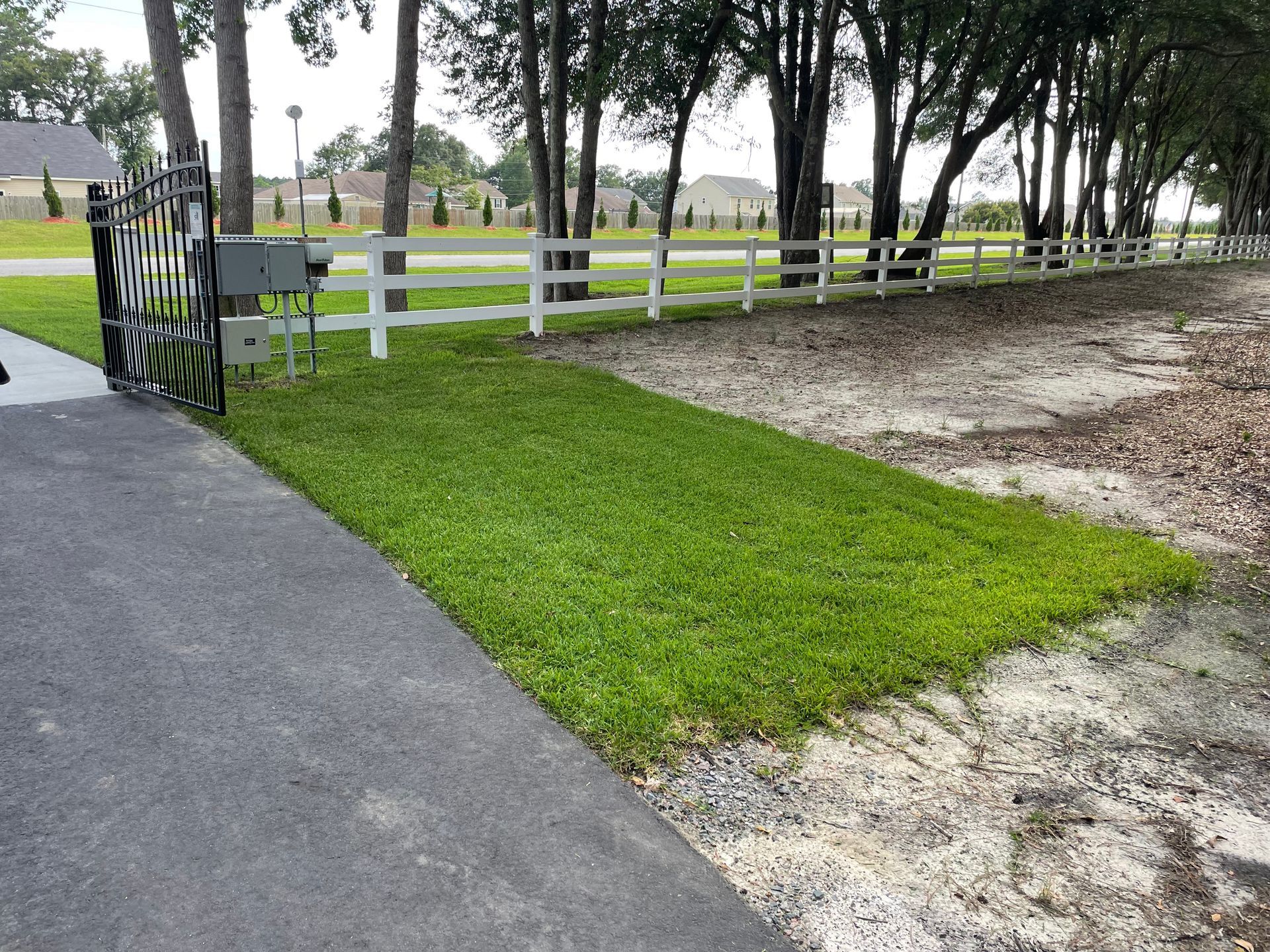 A white fence surrounds a lush green field with trees in the background.