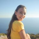 A woman in a yellow shirt is sitting on a hill overlooking the ocean.