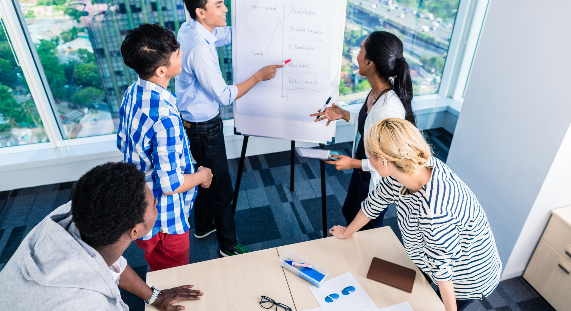 A group of people are sitting around a table looking at a whiteboard.