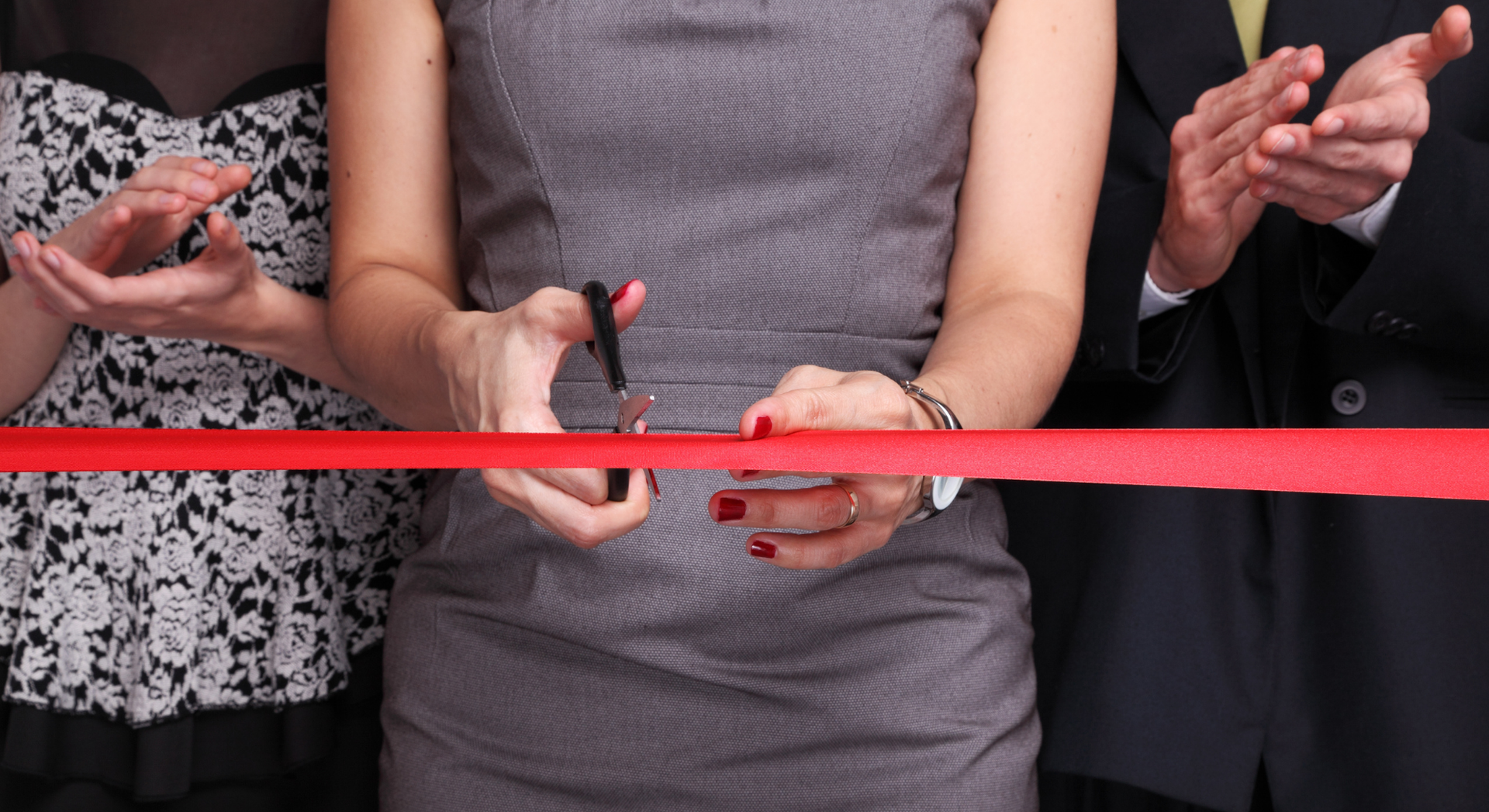 A woman in a dress is cutting a red ribbon