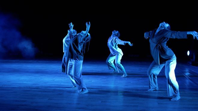 A group of people are dancing on a stage with blue lights.