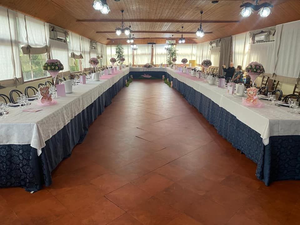 Lungo tavolo da banchetto a forma di U apparecchiato per una festa. I tavoli sono decorati con tovaglie bianche e centrotavola rosa e floreali.