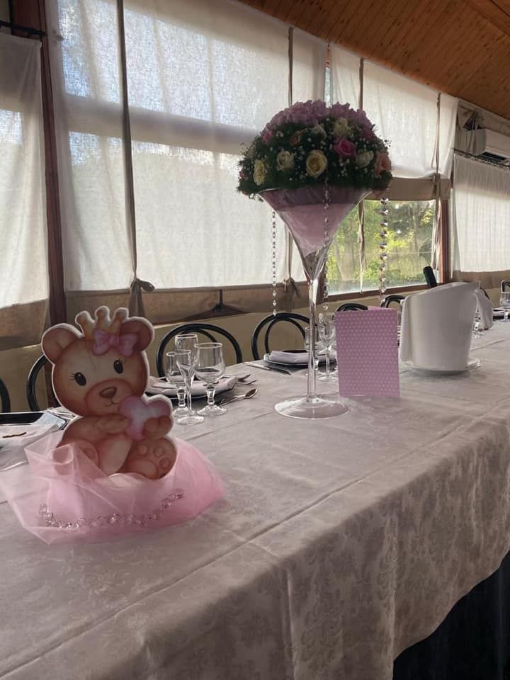 Tavolo apparecchiato per una festa con una decorazione a forma di orsacchiotto e un centrotavola floreale in un bicchiere da martini.