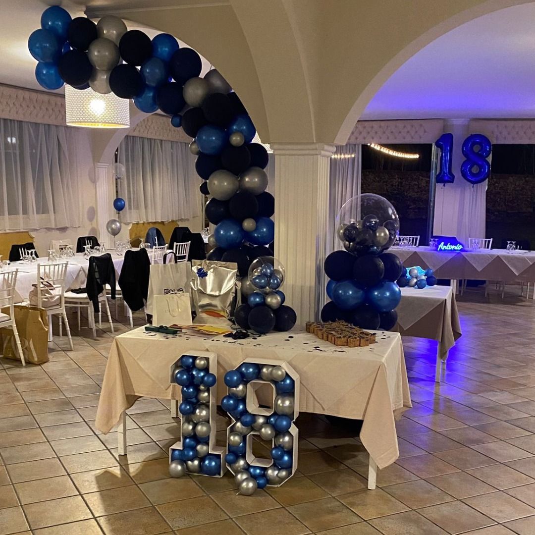 Festa per il diciottesimo compleanno. Palloncini argento e blu. Tavola apparecchiata con regali e torta.
