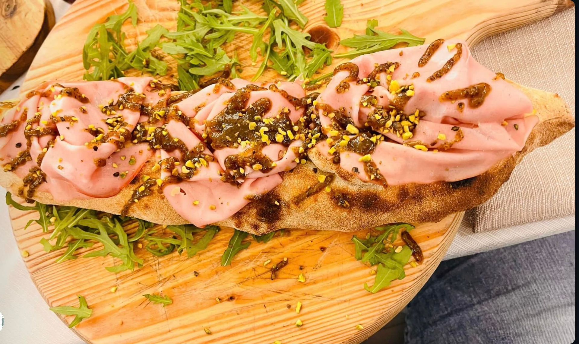 Panino aperto condito con carne affettata, salsa e rucola, servito su un tagliere di legno.