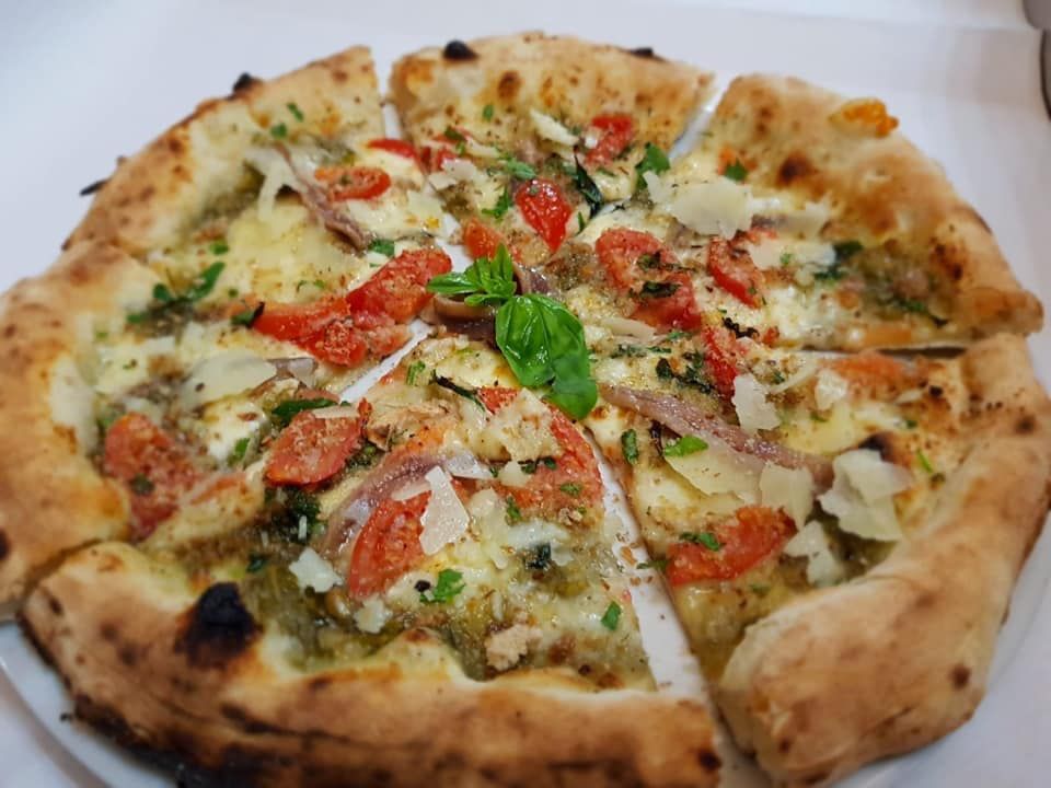 Pizza con pesto, pomodori e parmigiano, tagliata a fette.