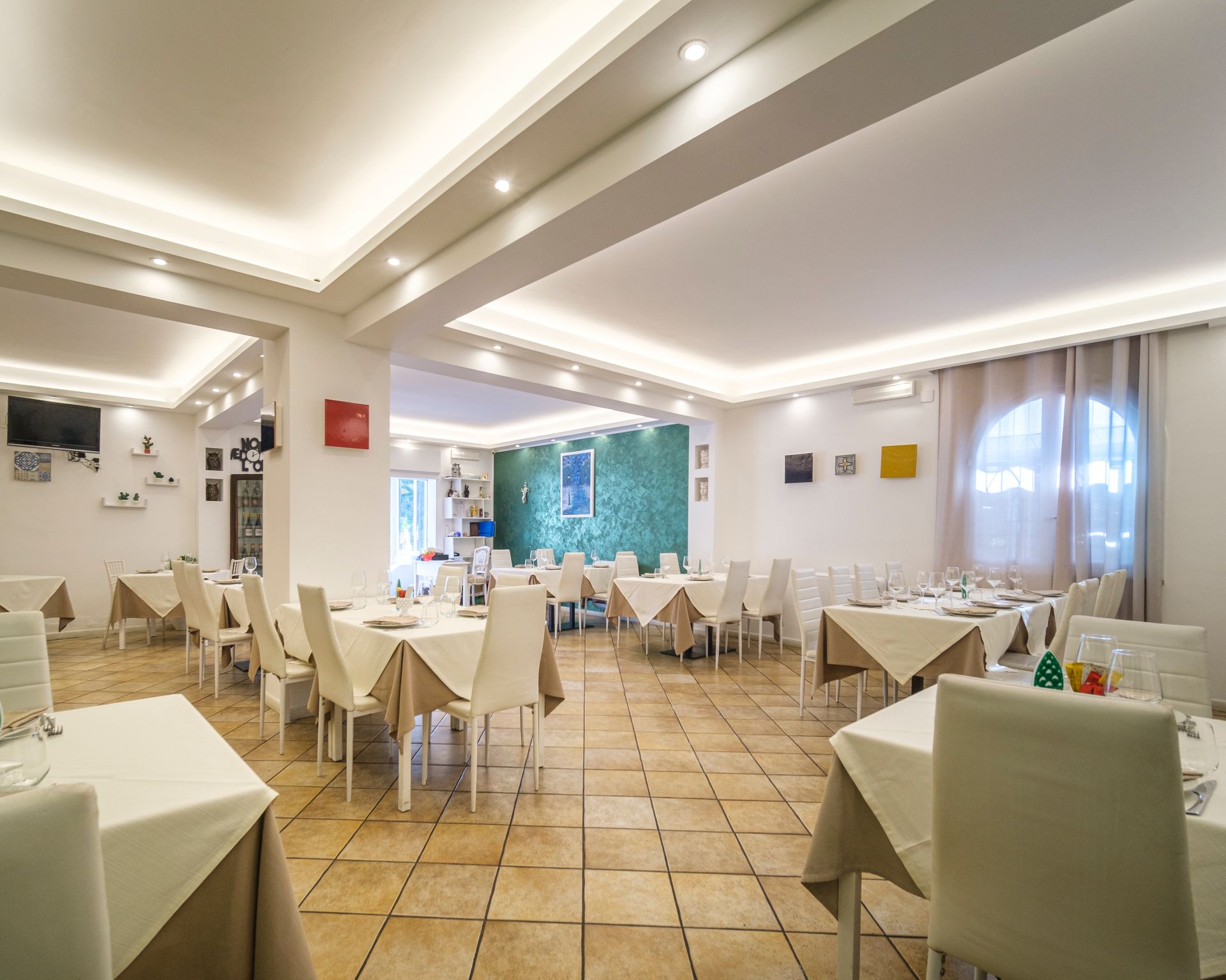 Interno del ristorante con tavoli quadrati, sedie bianche e una tavolozza di colori neutri.