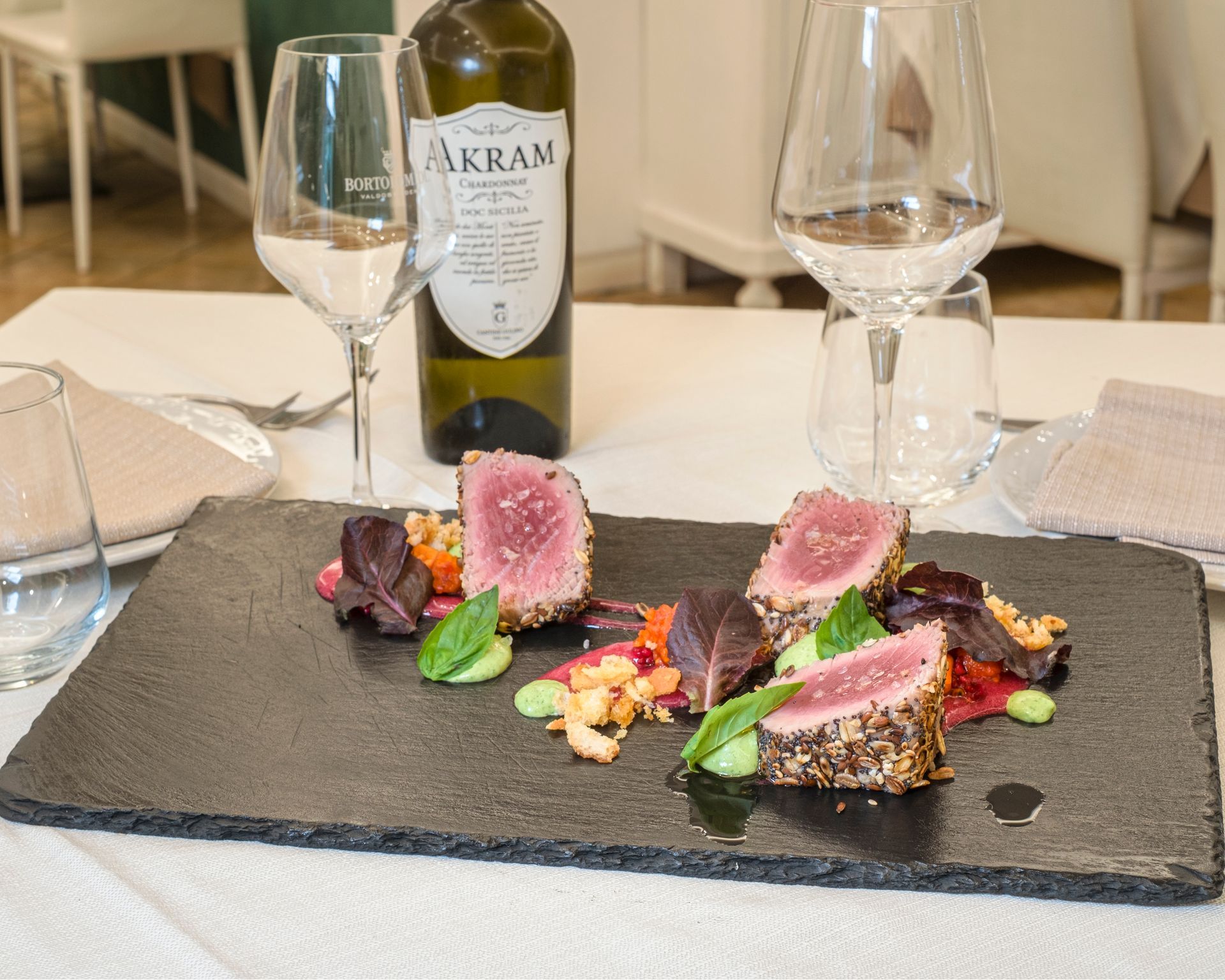 Piatto di tonno scottato su una lavagna nera, con barbabietole, salse e una bottiglia di vino in un ristorante.