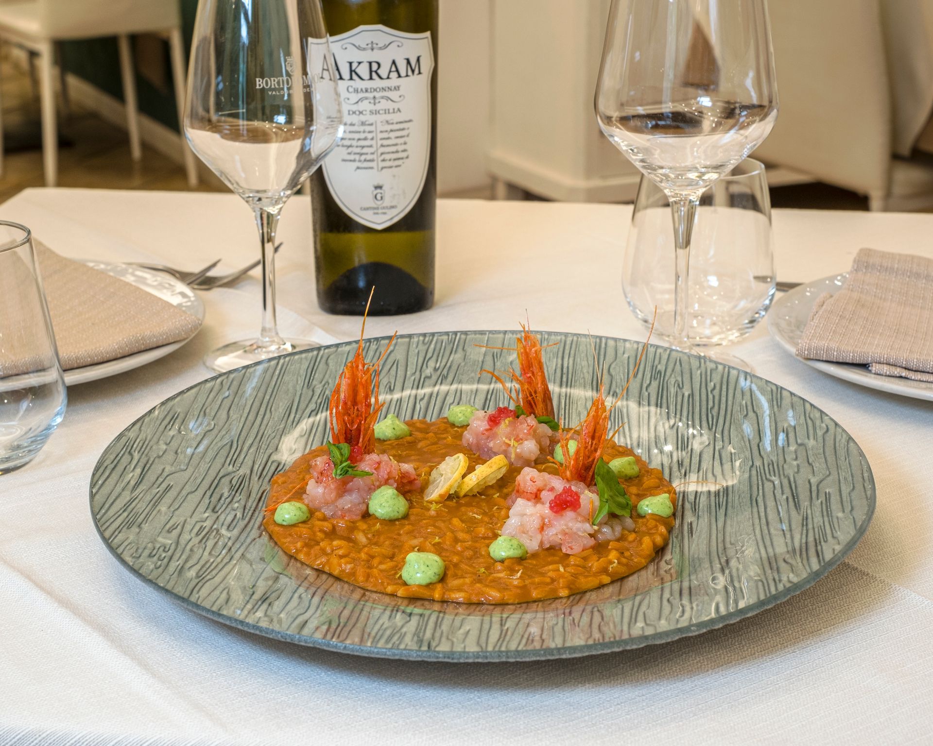 Piatto di risotto ai frutti di mare, con bicchieri di vino e bottiglia su una tovaglia bianca.